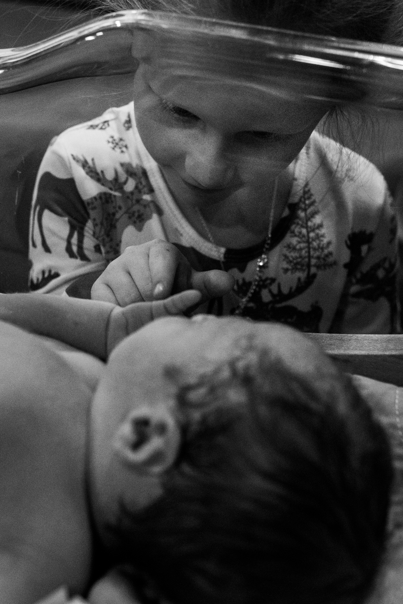 Older sister looking in at newborn baby brother in the crib at hospital