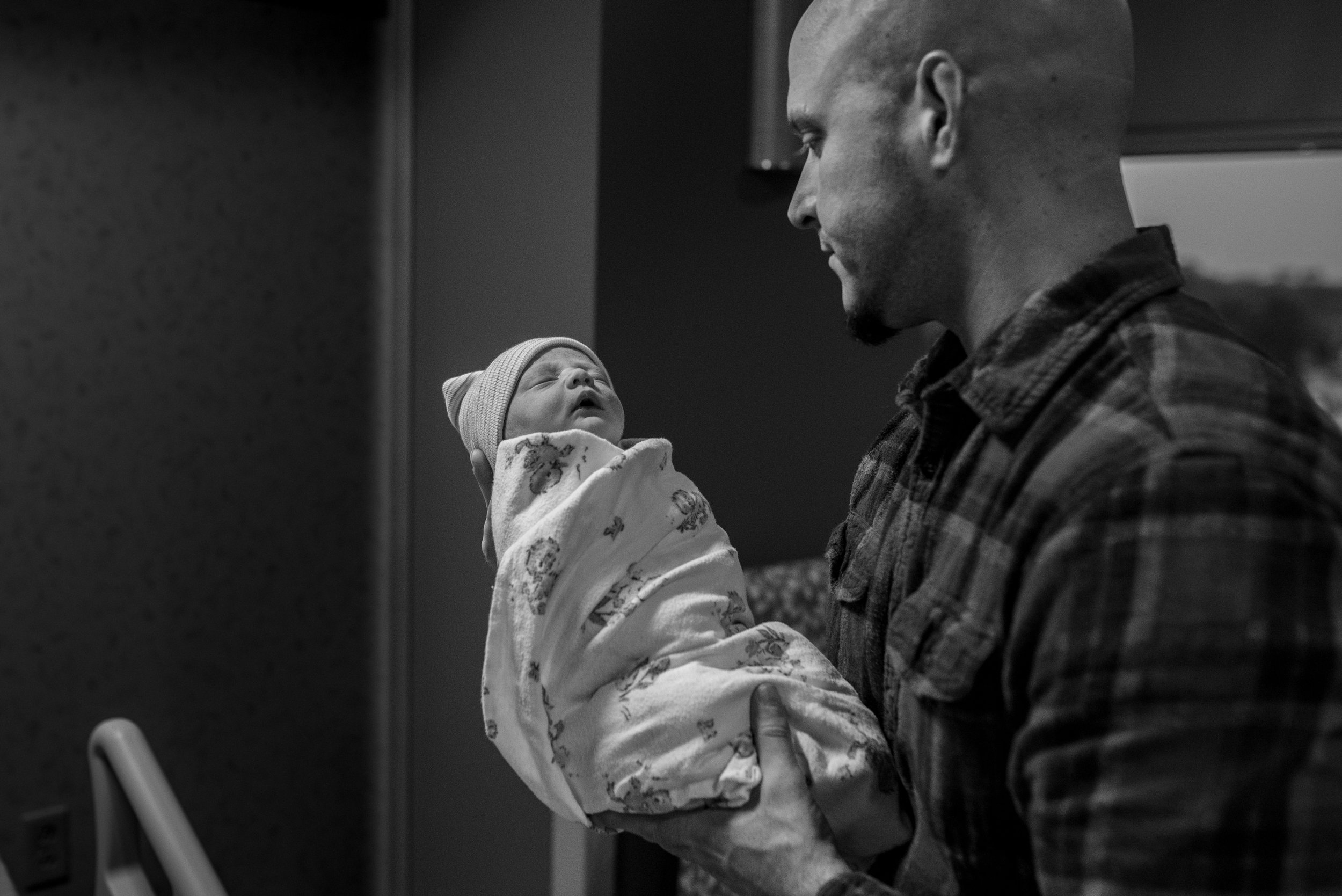 Dad holding newborn baby swaddled in a blanket in the hospital during milwaukee Fresh 48 session