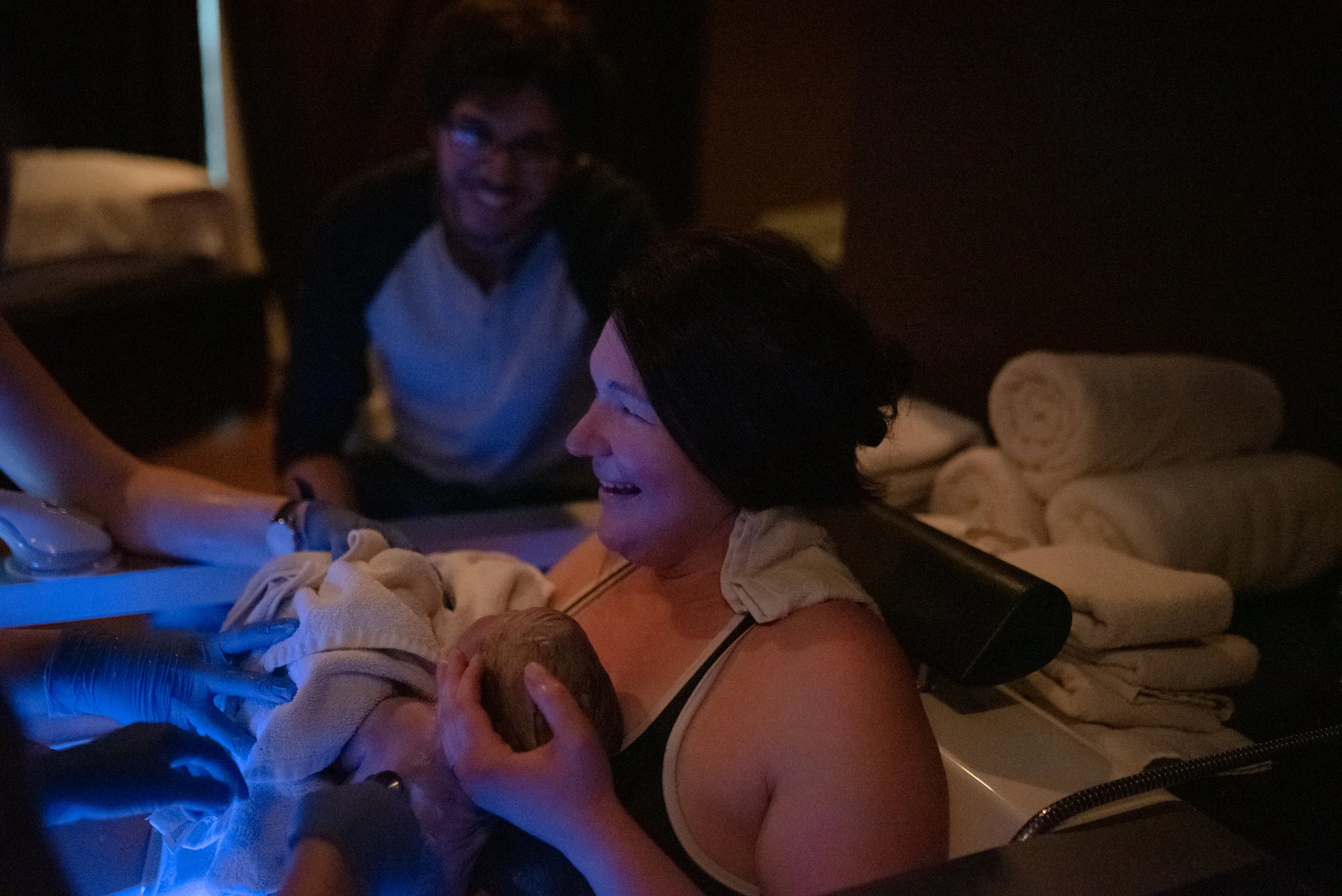 Smiling mom holds newborn baby in tub after delivery