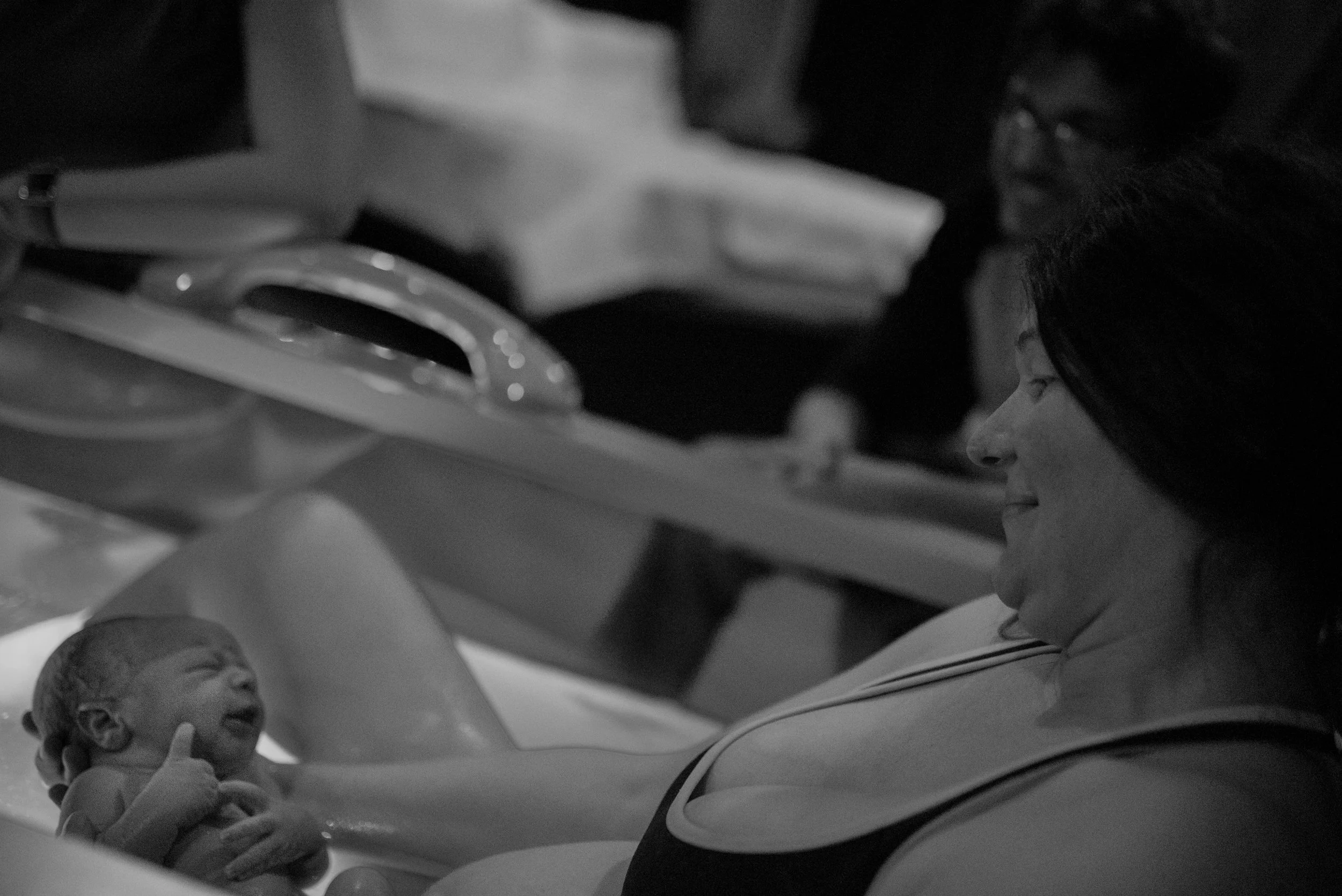 new mom looking down and smiling at newborn baby in tub