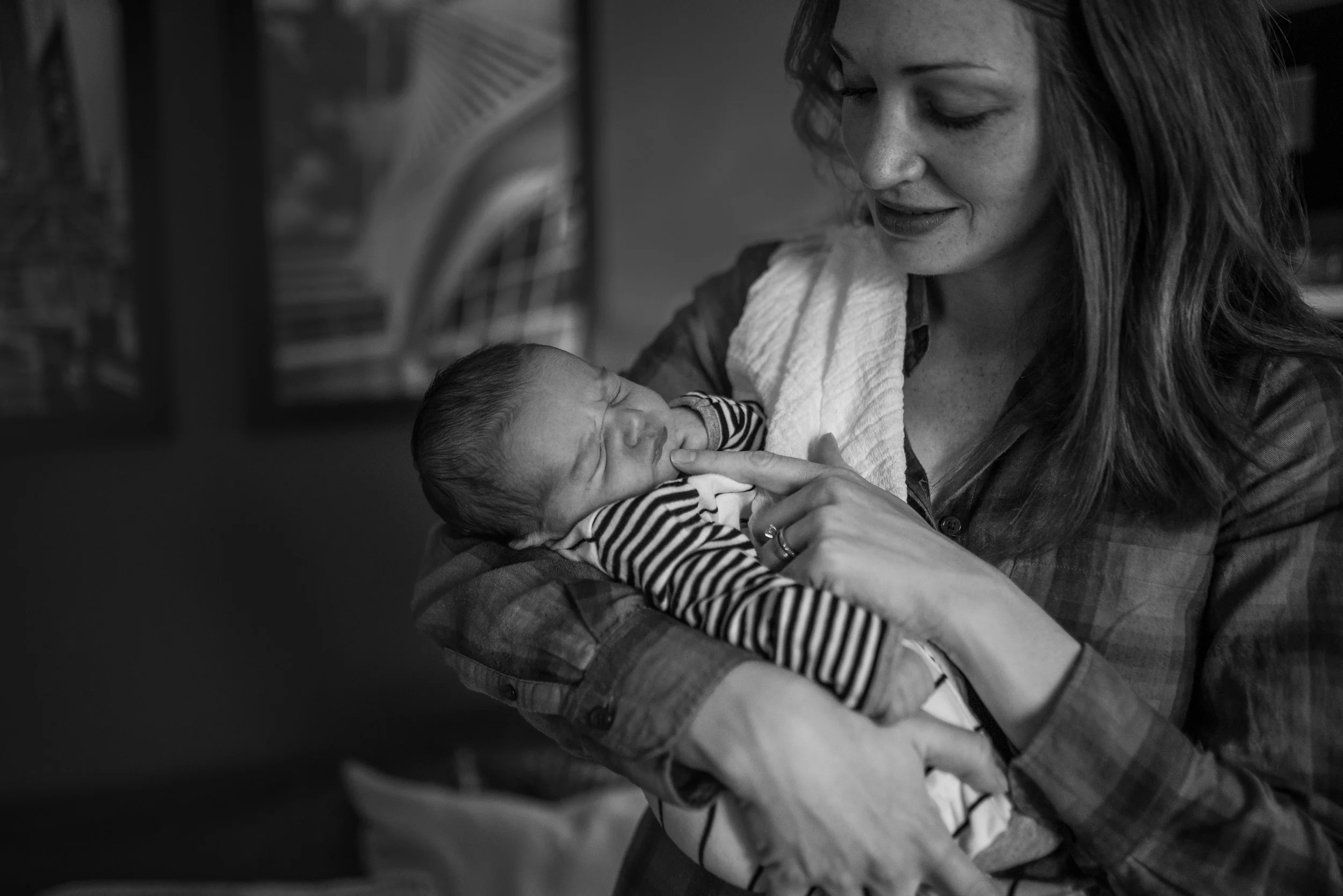 New mom holding newborn baby and looking at baby lovingly poking his chin with her finger