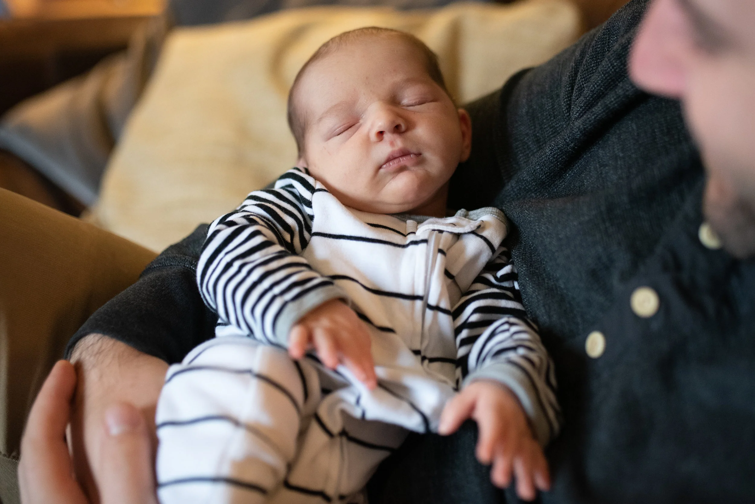 Newborn baby sleeping in dads arms on the couch in stripped pajamas