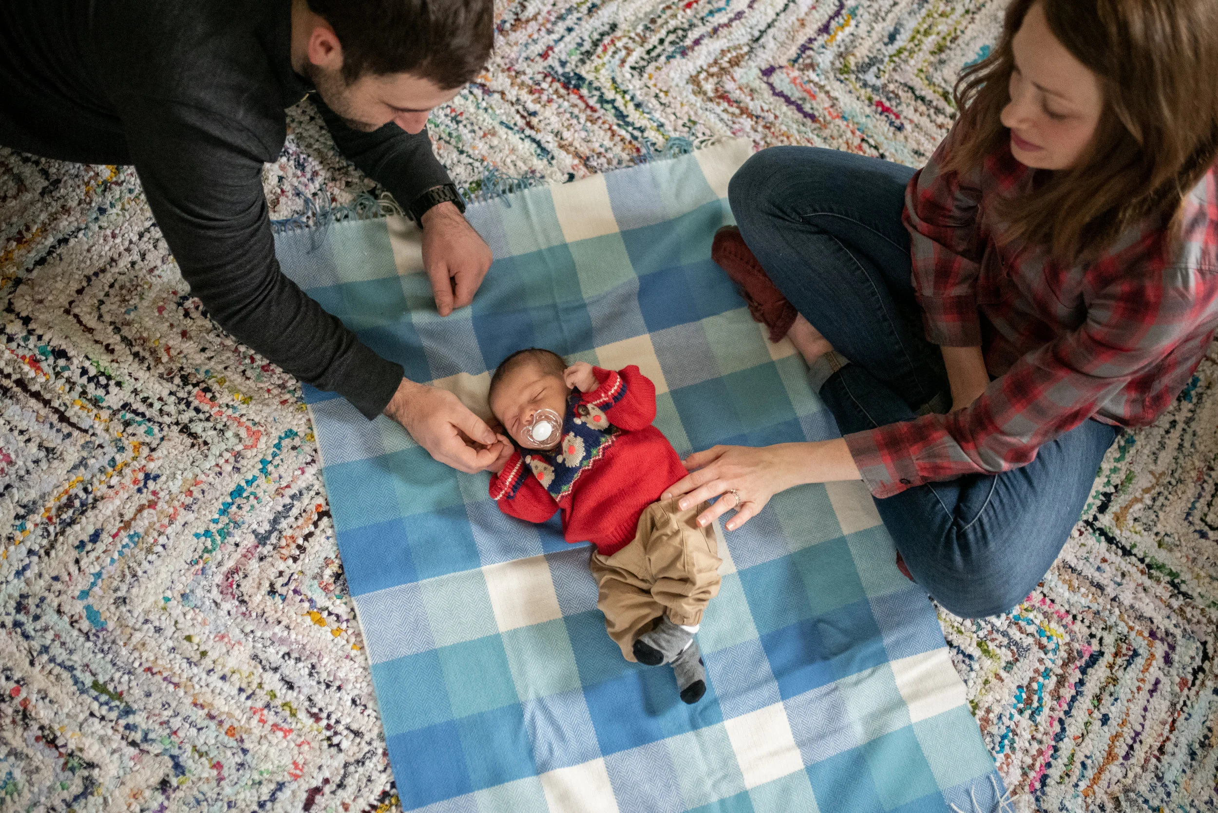 Newborn baby laying on blanket on the floor mom and dad are both gently touching him