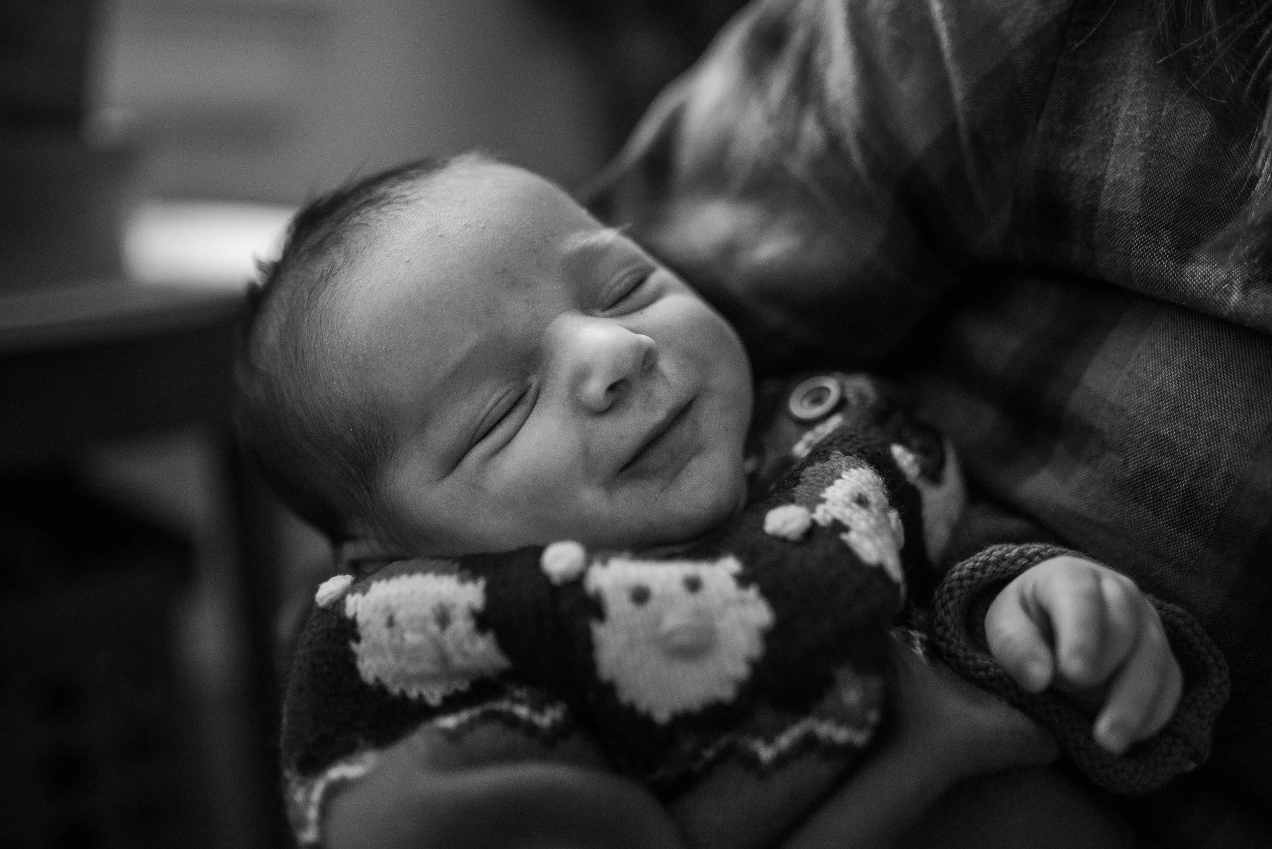Newborn baby smiling with eyes closed wearing a Santa sweater