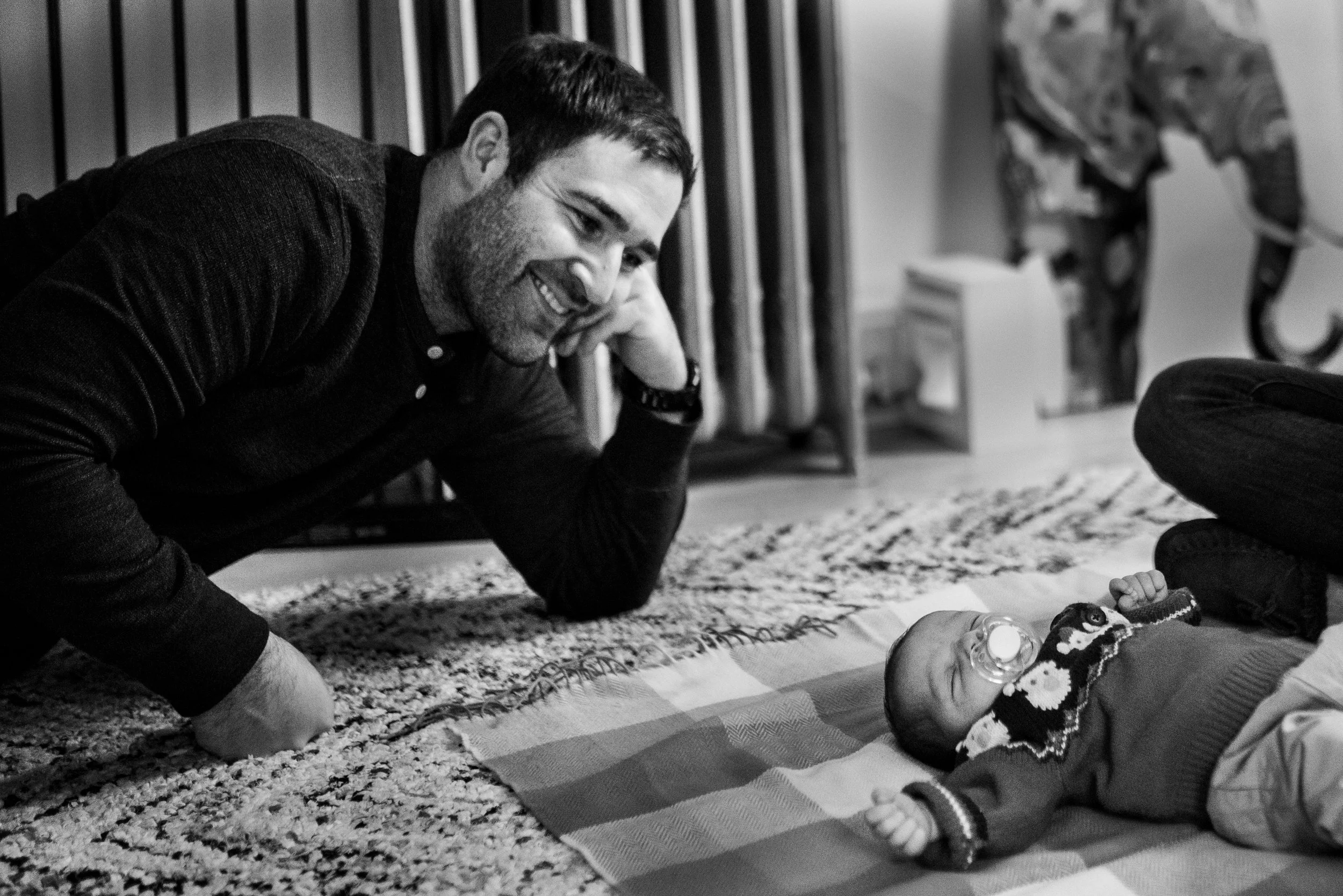 Newborn baby sleeping on the floor with pacifier in his mouth, dad looking down and proudly smiling at baby