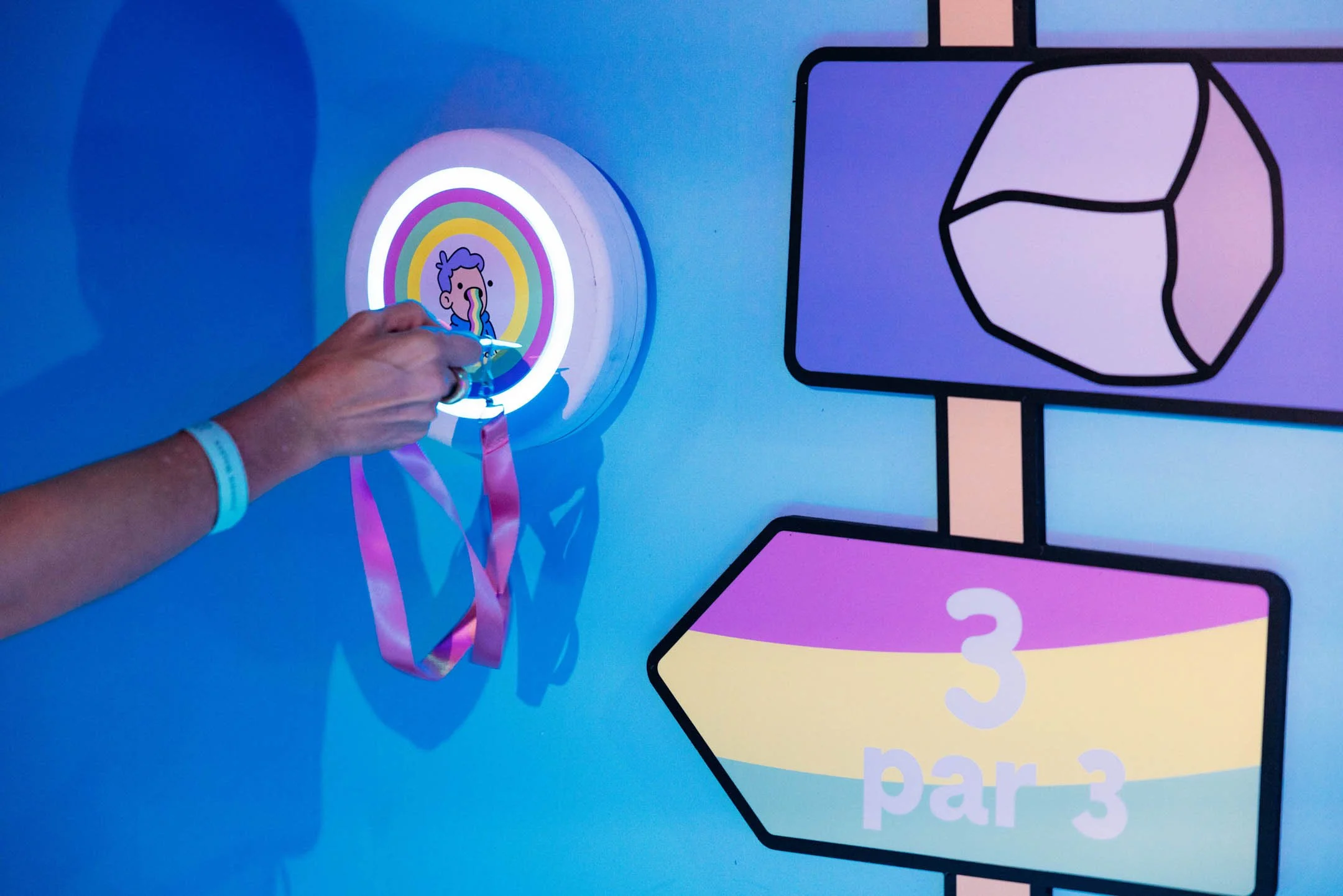Person sliding a rainbow-colored medal with a cartoon character and rainbow design on a blue wall.