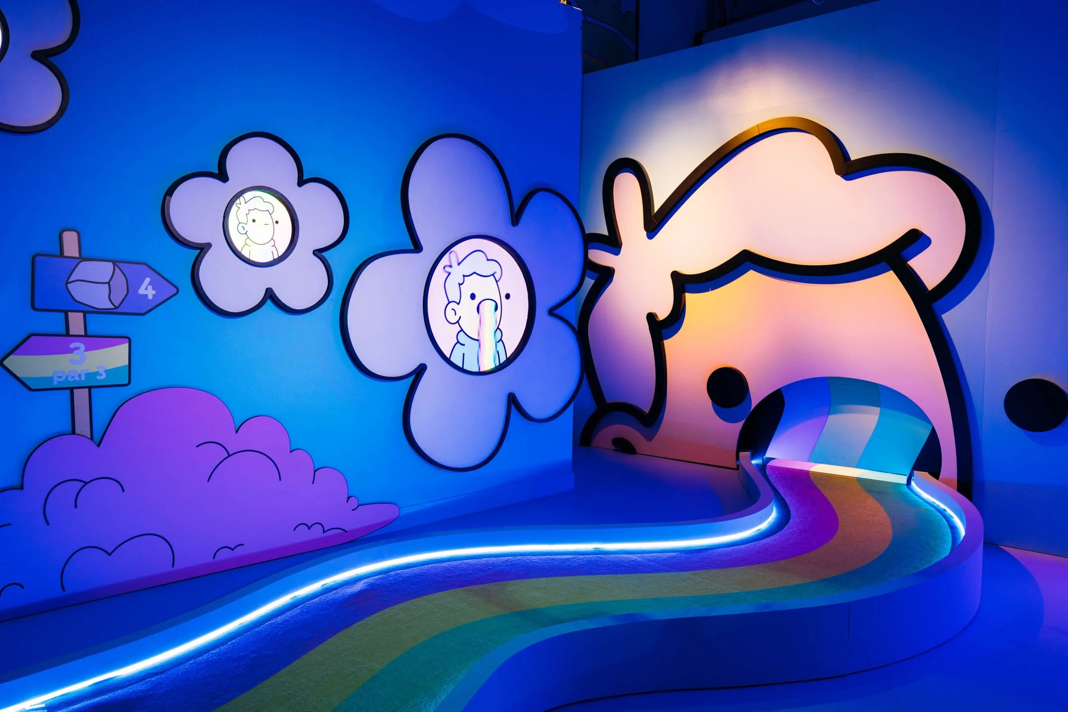 Colorful indoor scene with rainbow pathway, large cartoon dog face entrance, and fluffy clouds with funny faces on the wall. Decorations include signs indicating hole numbers and par in a miniature golf course.