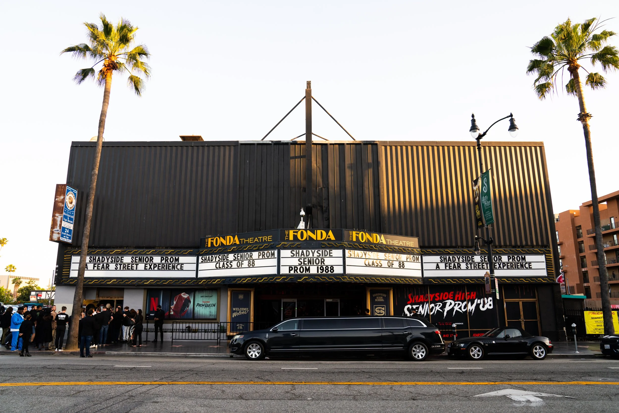 Exterior of the Fonda Theatre with marquee displaying upcoming events, including high school prom and senior class of 88, with people gathered outside and cars parked in front.