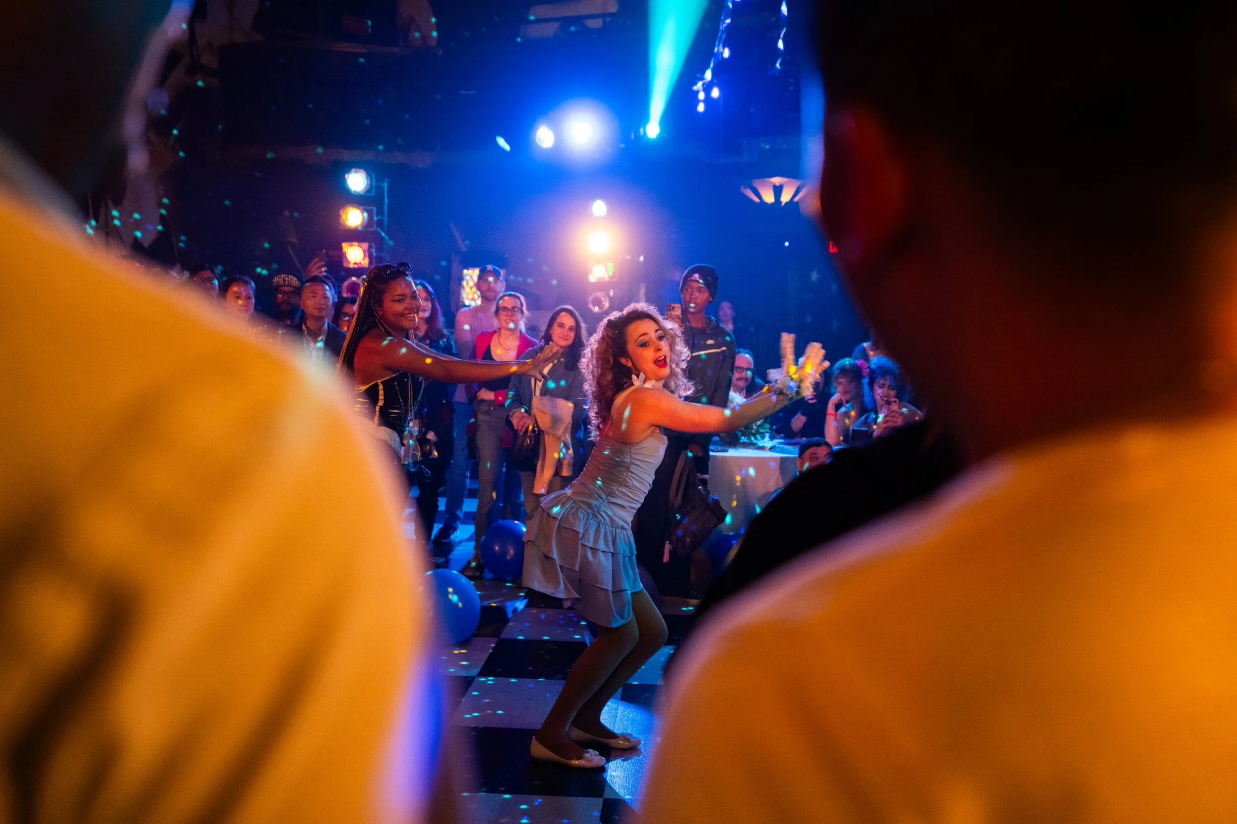 A woman dancing on a dance floor with colorful lights, surrounded by a crowd of people at a lively party or celebration.