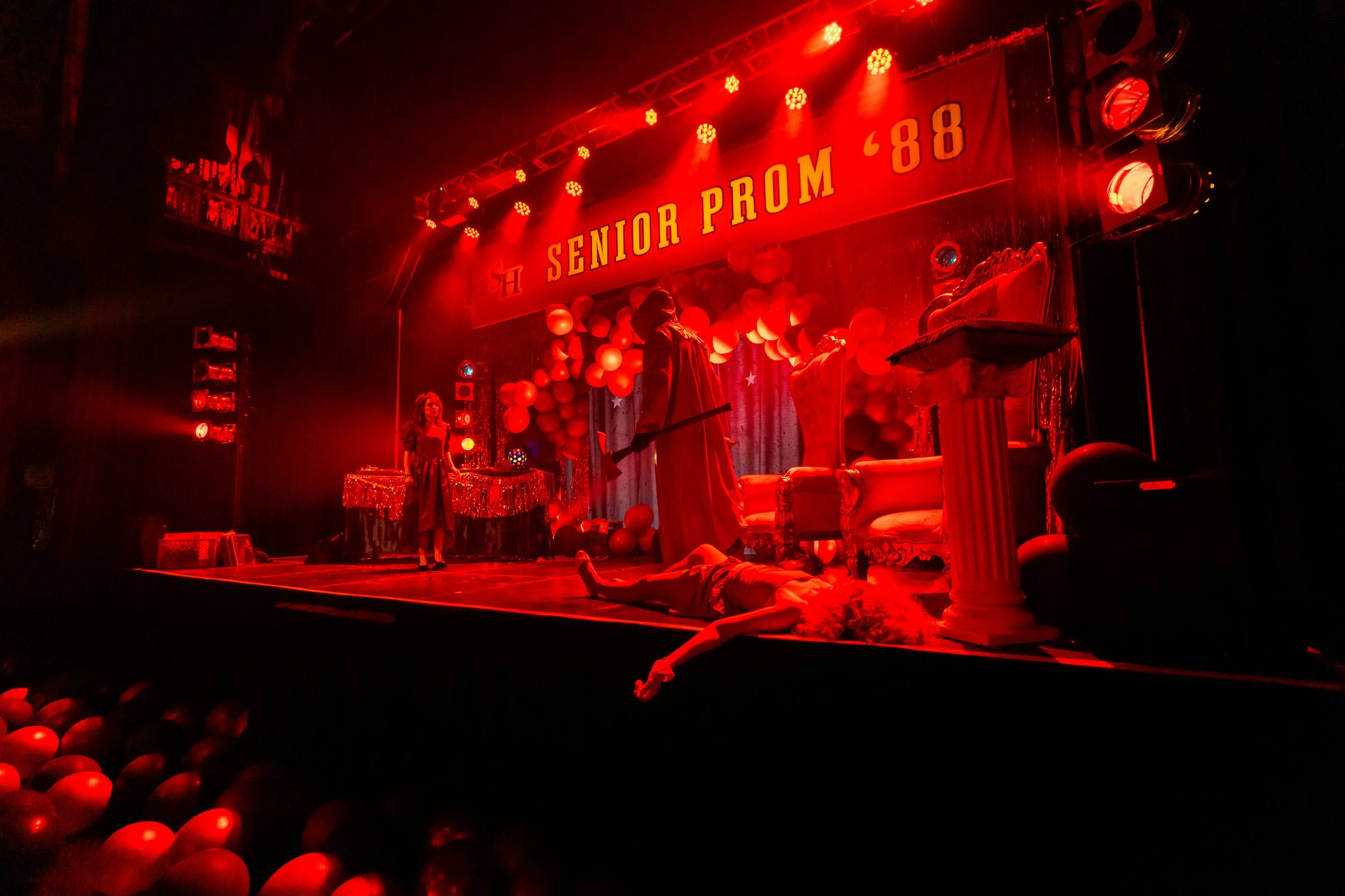 Stage decorated for a senior prom with red lighting, balloons, chairs, and a banner that reads 'Senior Prom '88'.