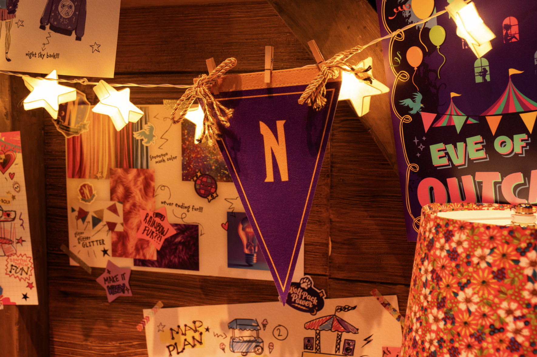 Decorative triangle pennant with the letter 'N', illuminated by star-shaped string lights, with various colorful posters and drawings on the wooden wall behind, in a festive setting.