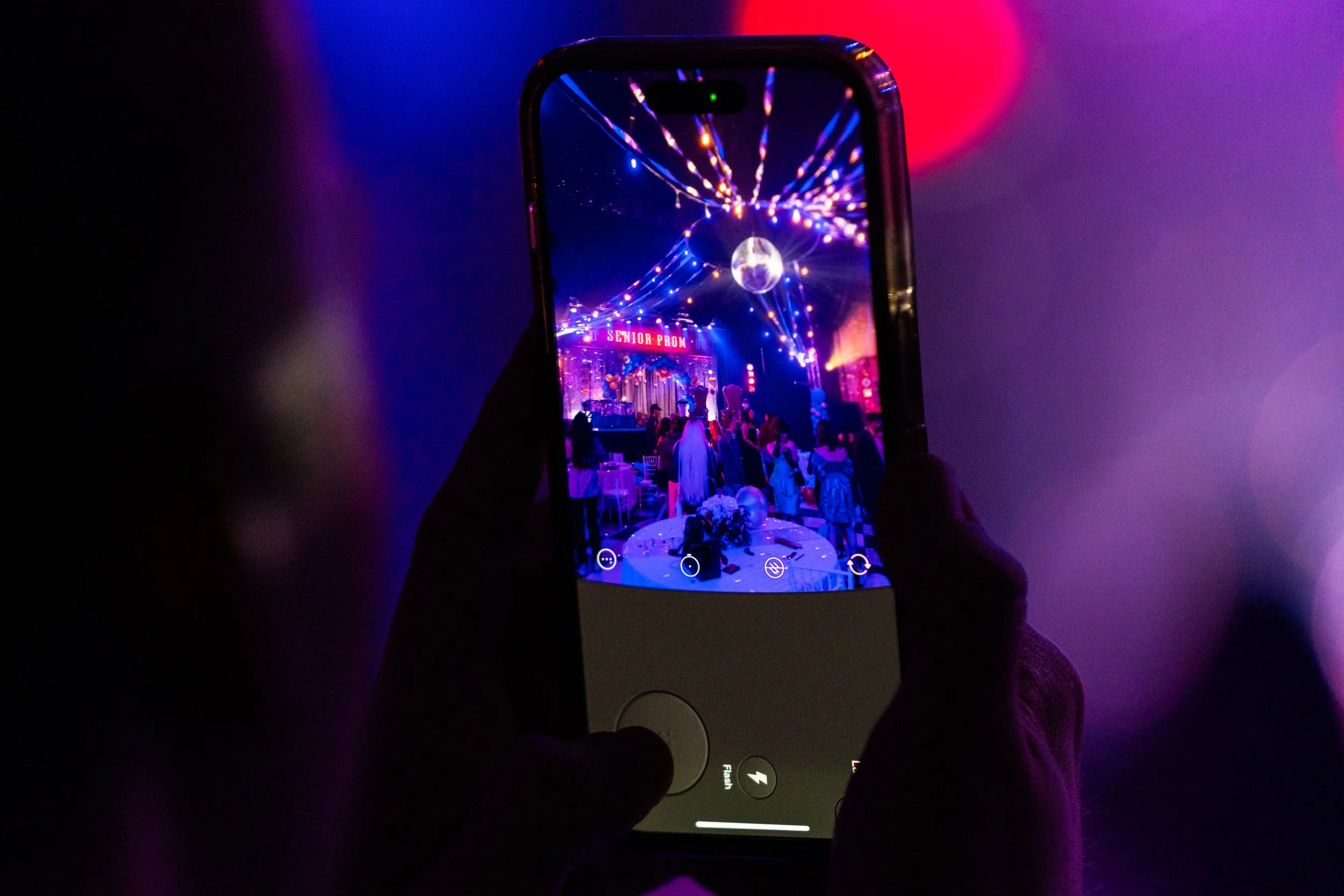 Person taking a photo of a decorated event with a smartphone in a dark, colorful environment.