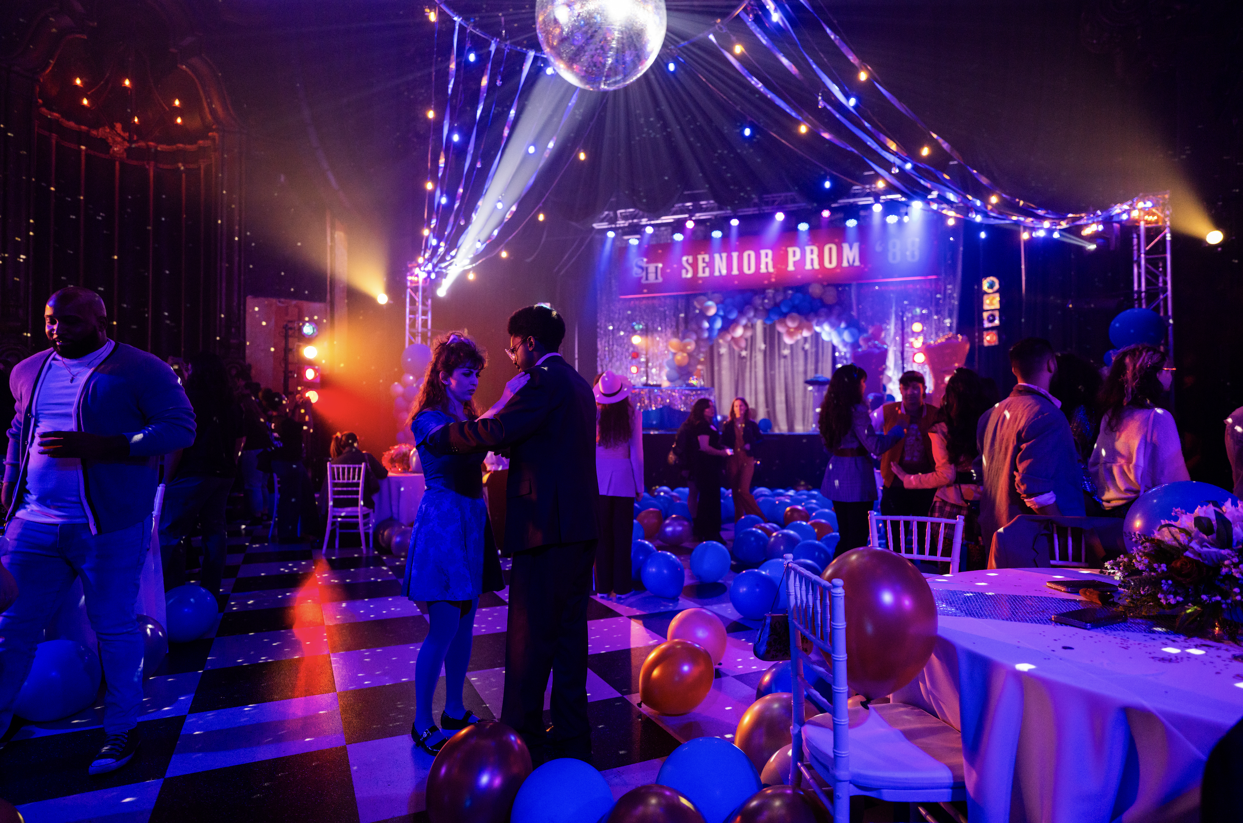 A lively senior prom celebration with colorful balloons, stage lighting, and students dancing and socializing inside a decorated venue.