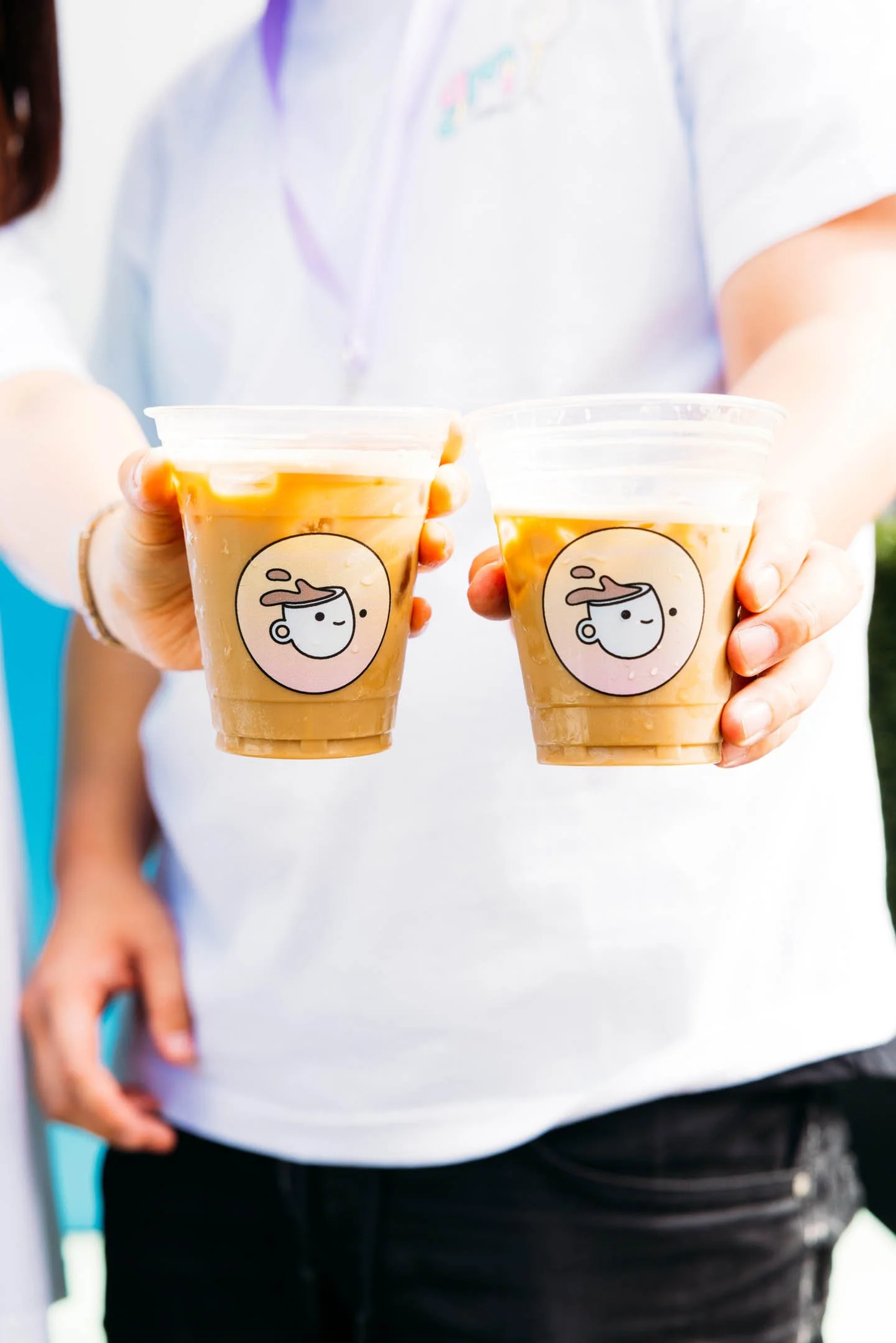 Two people holding cups of iced coffee with a cartoon logo of a smiling face with steam rising from the head.