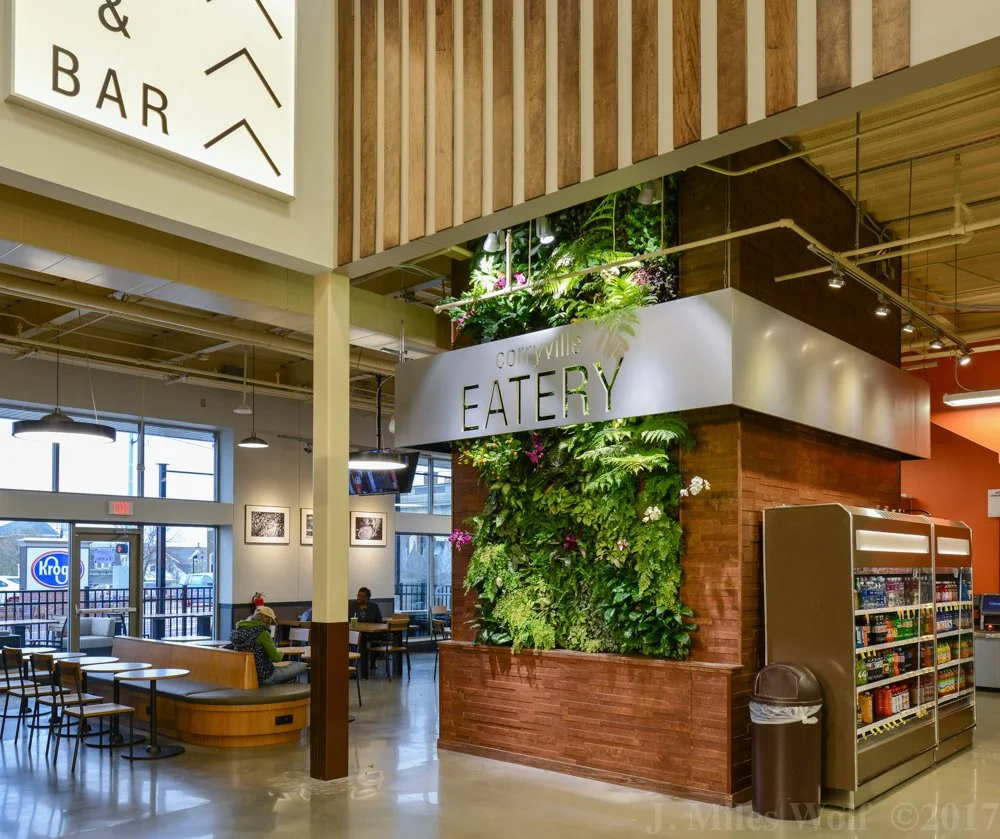 Interior of a modern eatery in a Kroger with a green wall, a vending machine, and a seating area with customers.