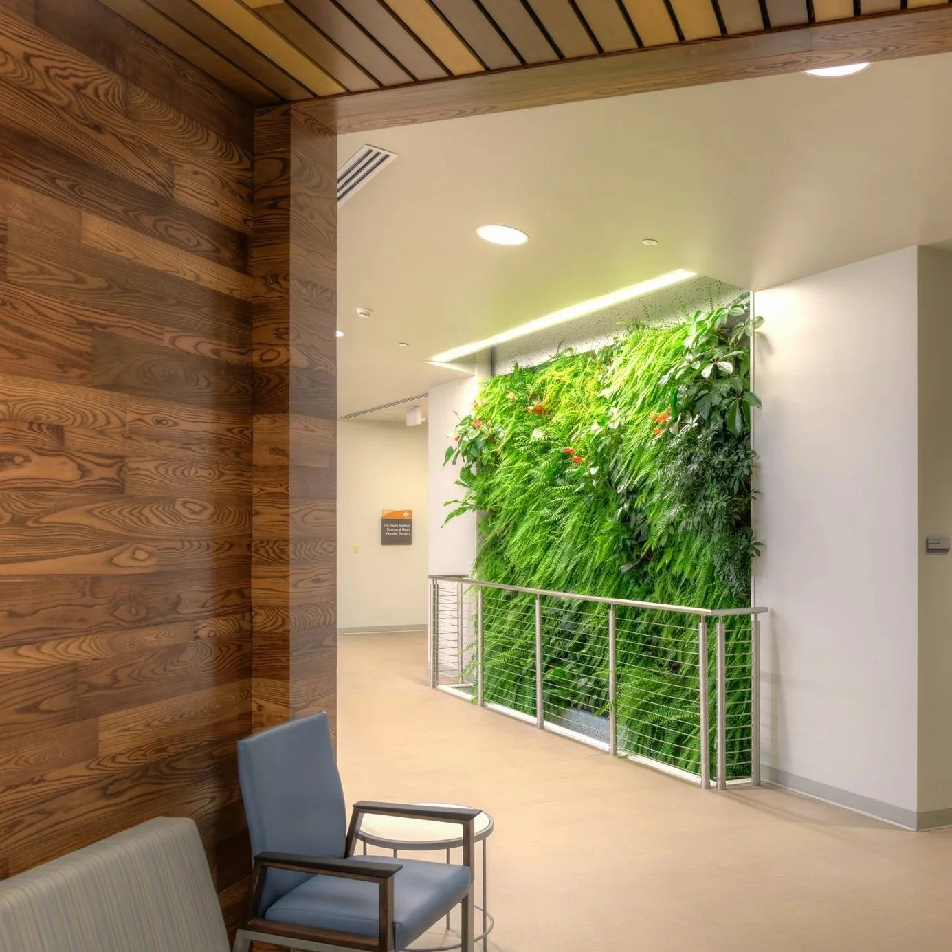 Indoor space with a wooden paneled wall, a green vertical garden on the wall, and seating including a gray chair with wooden arms.