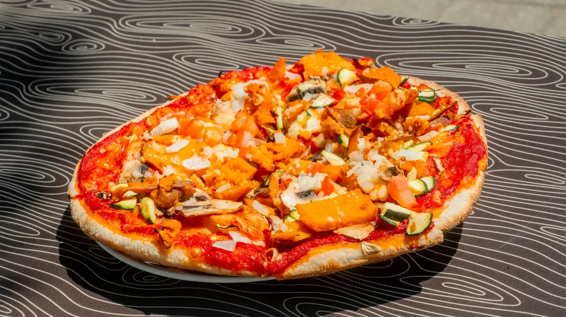Stone-baked vegan pizza from Night Kitchen in Peterborough topped with fresh vegetables and dairy-free ingredients, available for pickup or delivery.