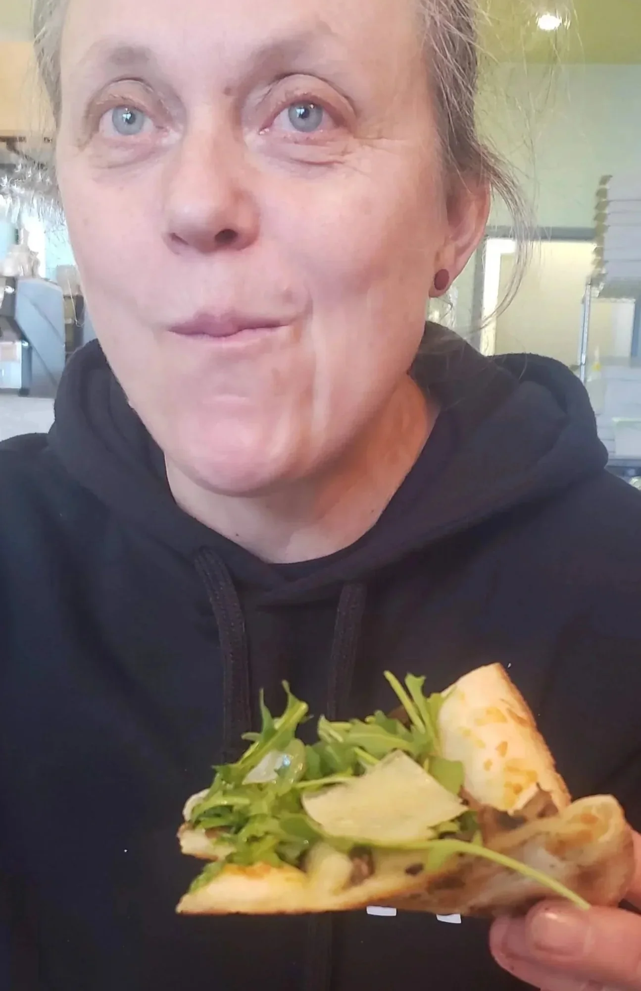 Night Kitchen owner holding a pizza slice topped with leafy greens.