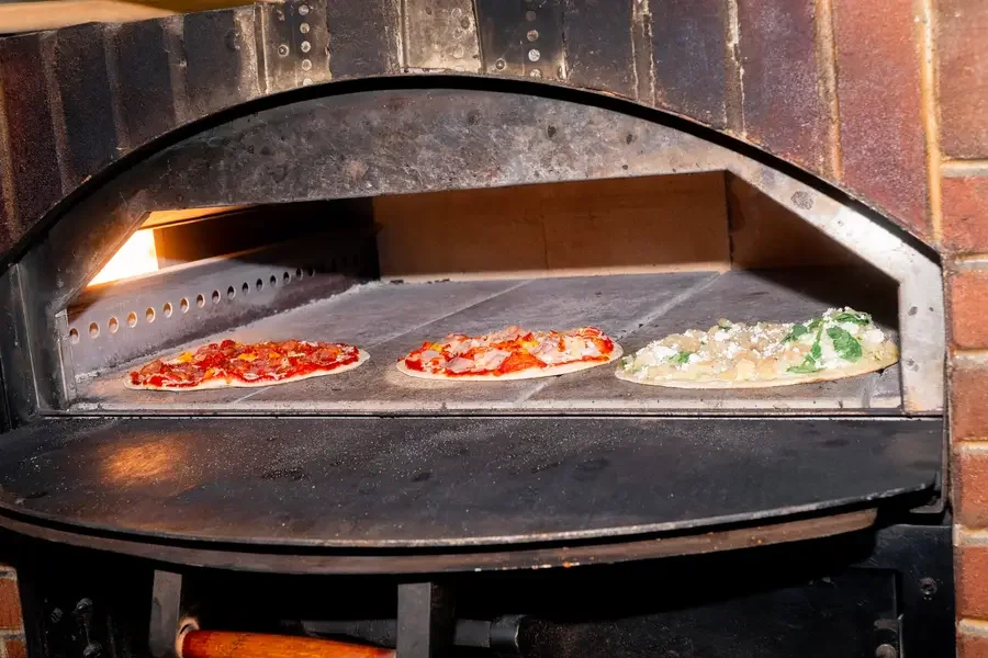 Three pizzas baking together on the stone hearth of the Night Kitchen oven.