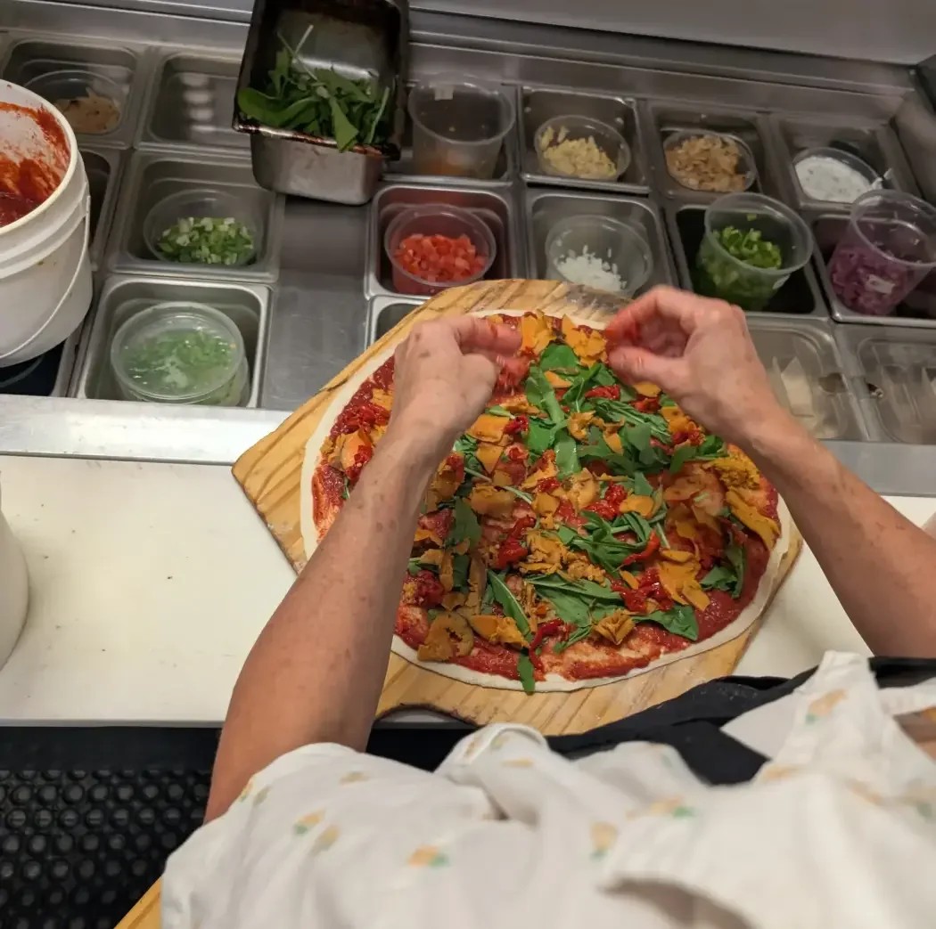 Leafy greens being added to a vegetable pizza at Night Kitchen.