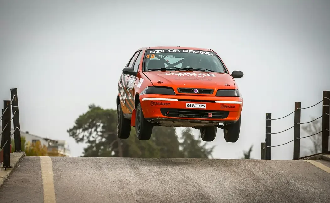 Red rally car airborne over a country road.