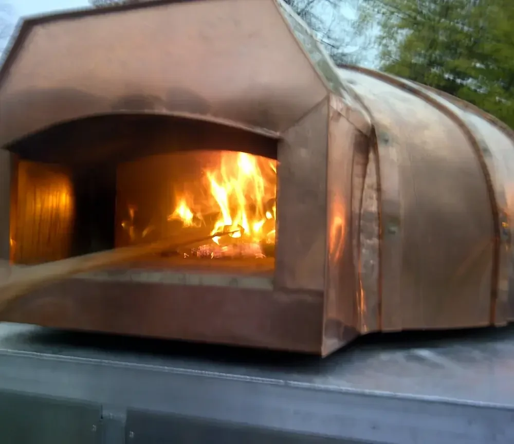 copper mobile pizza oven with raging fire inside