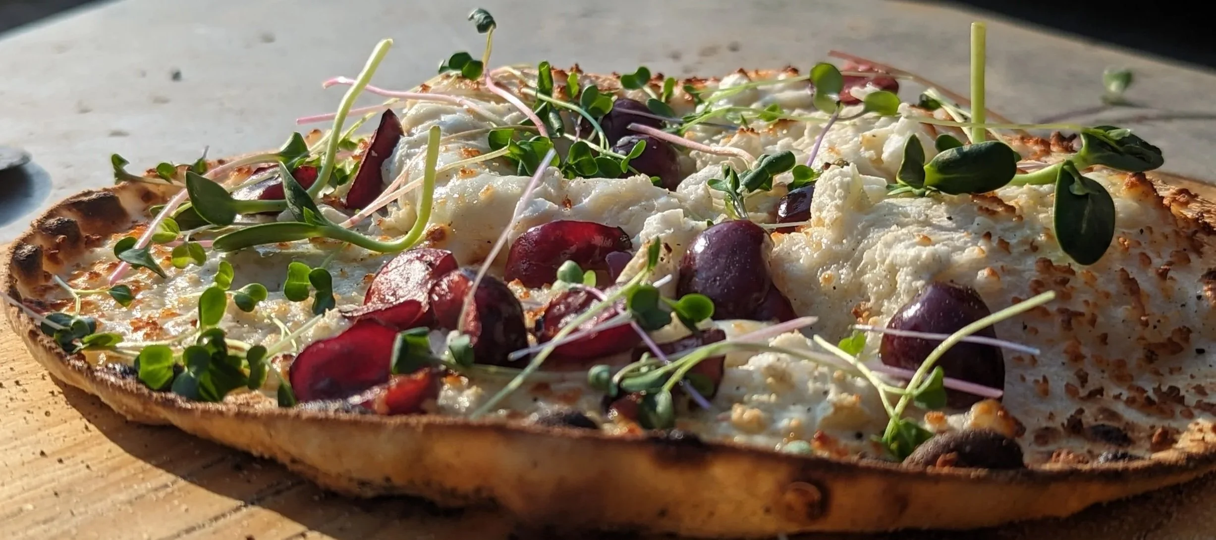 Finished Night Kitchen pizza with a crisp stone-baked crust, cheese, cherries and microgreens