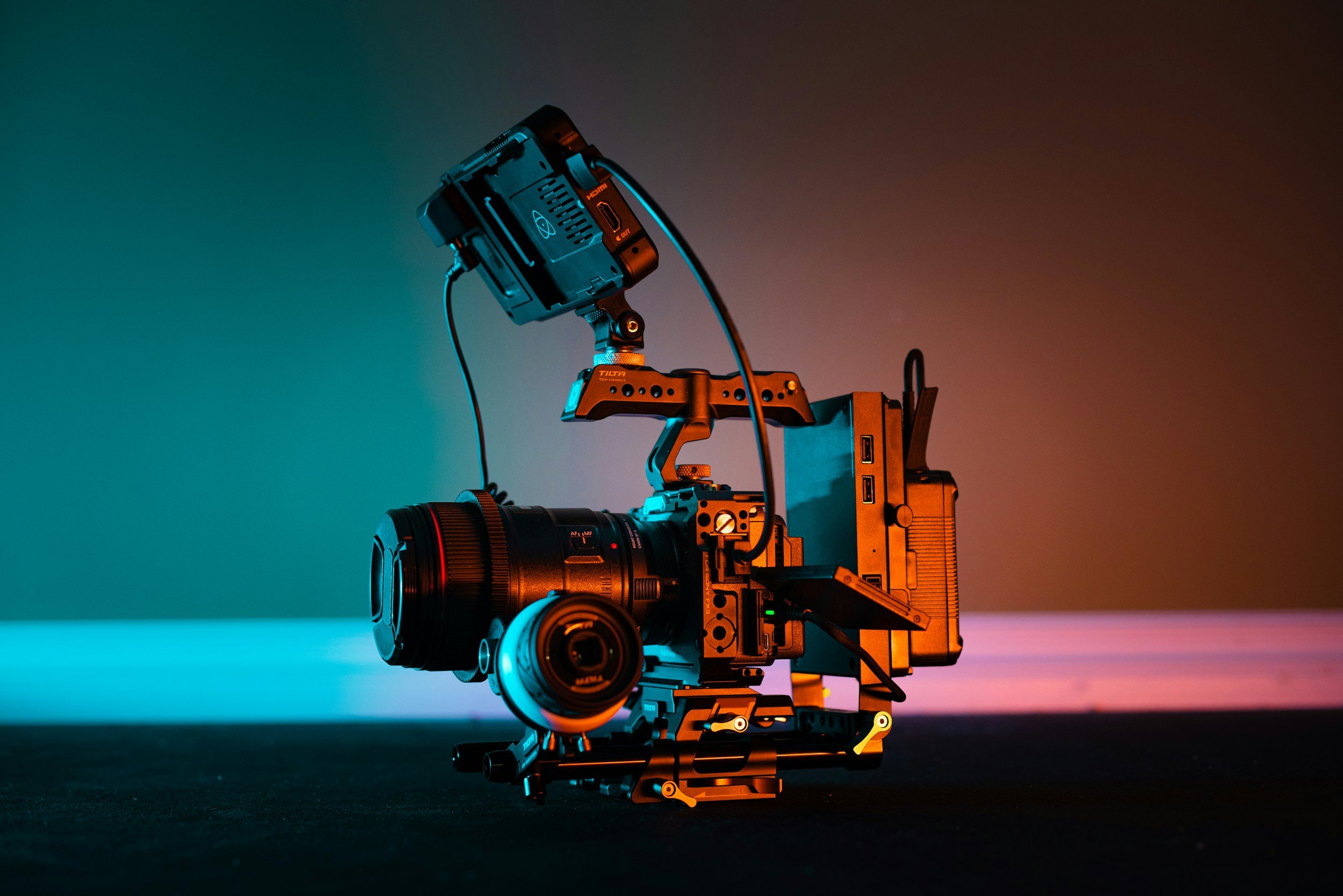 A professional cinema camera setup with accessories, illuminated by colorful ambient lighting in a studio setting.