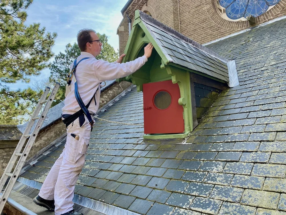 Dave Asseler werkt aan het schilderwerk van een kerkdakkapel
