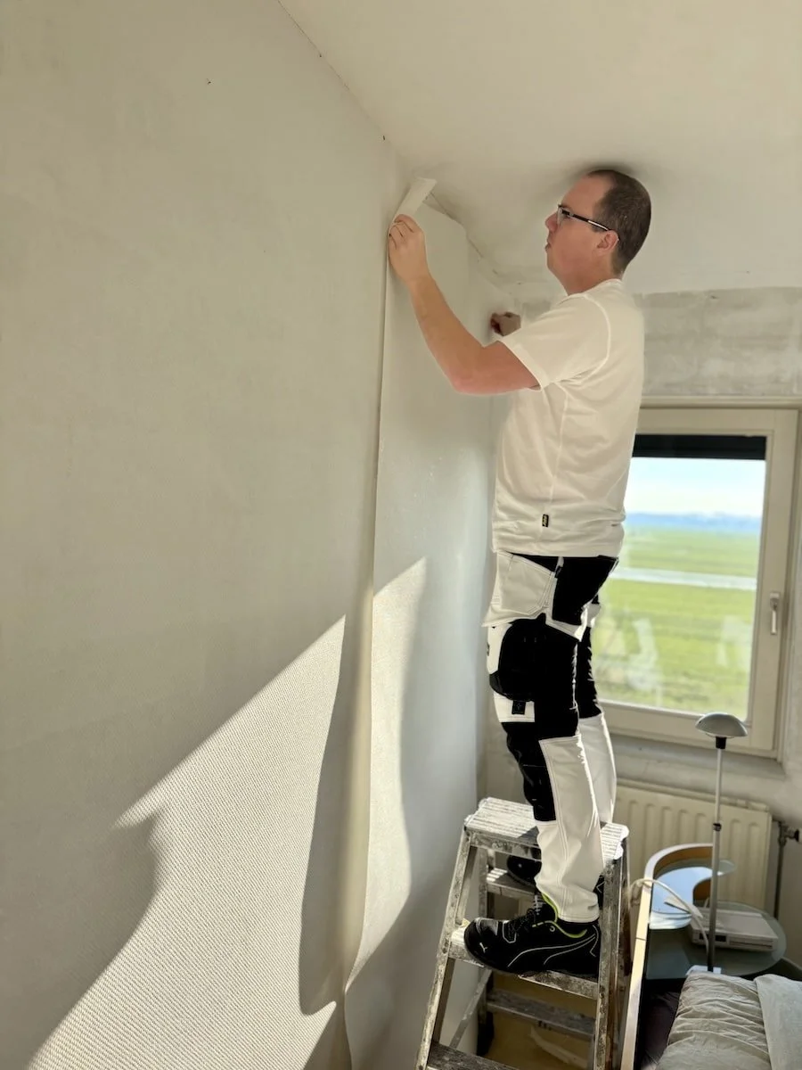 Dave Asseler plakt een baan glasvezelbehang – Vakkundige wandafwerking door Schildersbedrijf E.G.M. Asseler & Zoon voor een strak en duurzaam resultaat