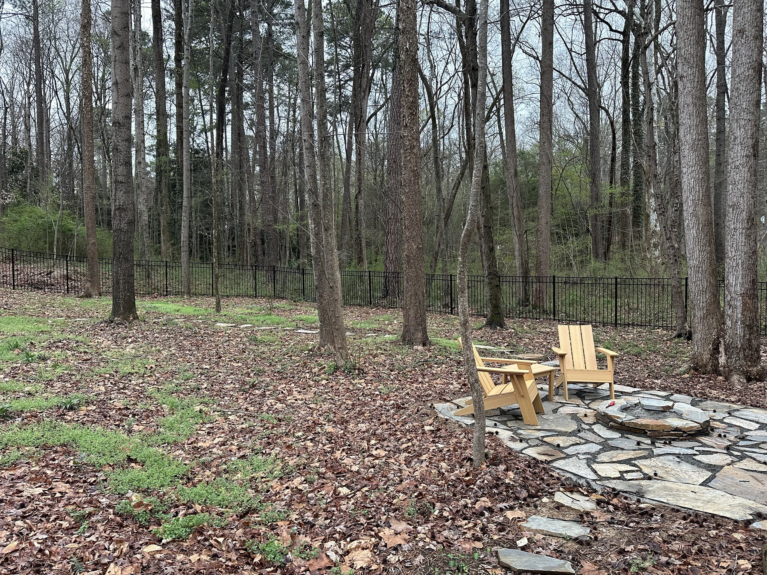 forest with mature trees and a fire pit made large stone that is sitting on a flagstone patio with adirondack chairs