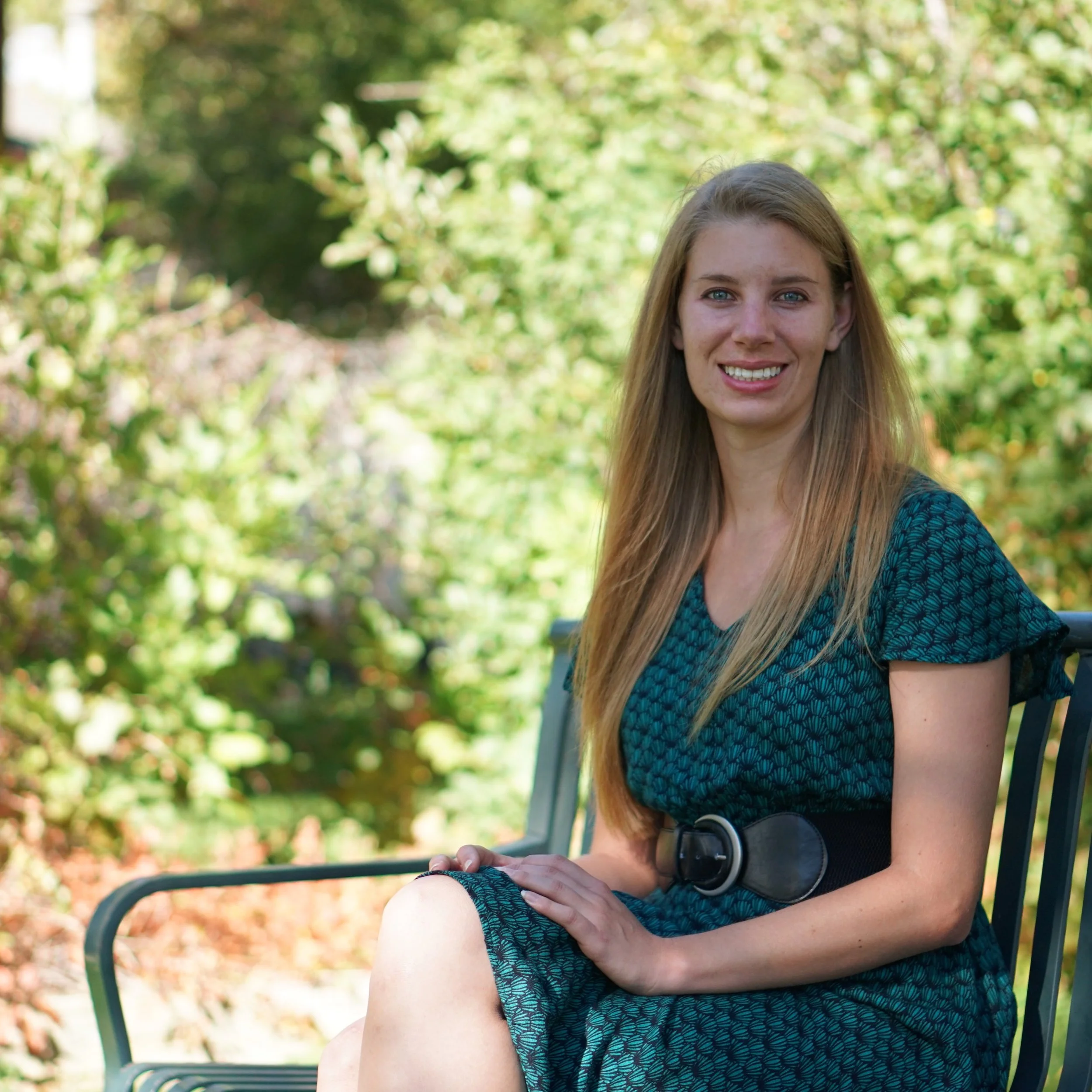 Caitlin Berve sitting on a park bench in a green dress