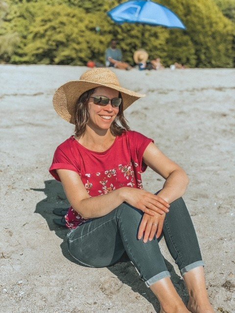 Casey on a beach in a sunhat and red shirt.