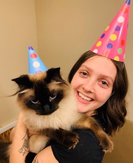 Carmen in a birthday hat holding a cat also in a birthday hat 