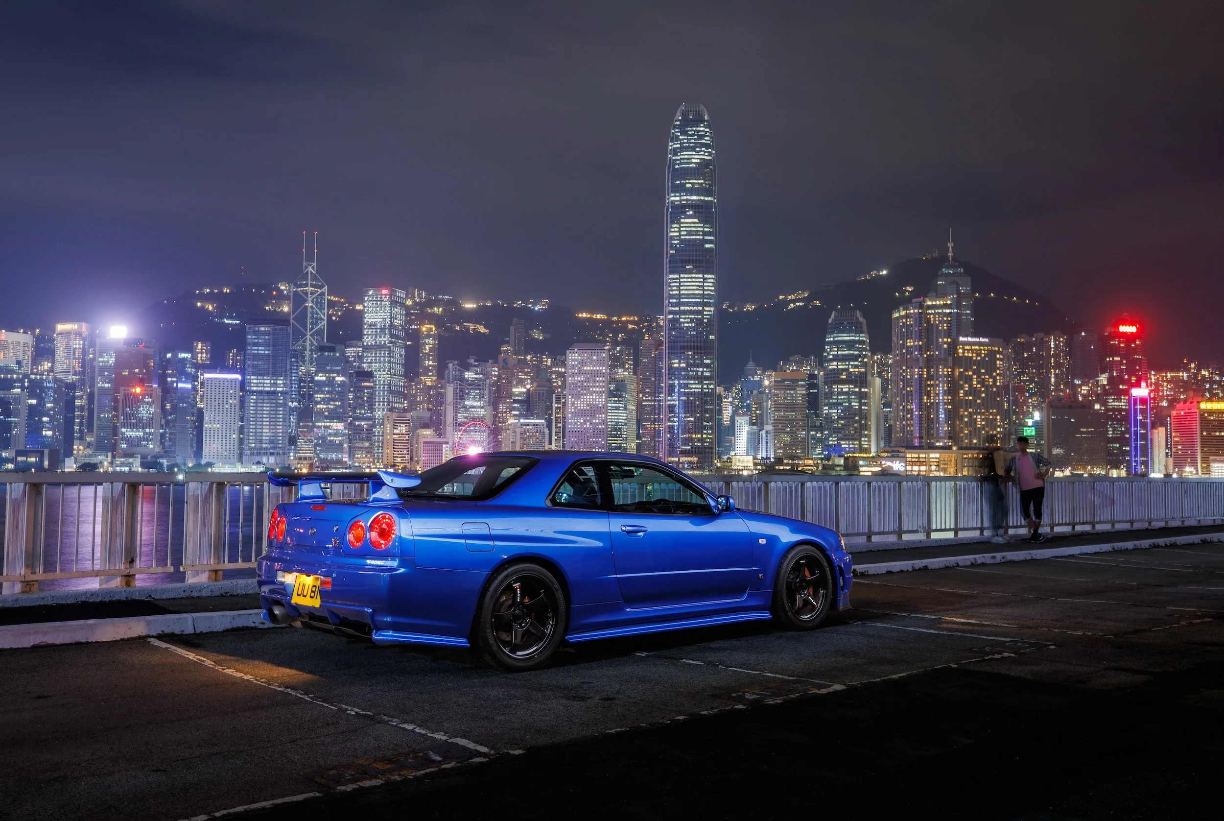 Photo by Larry Chen of a Nissan R34 Skyline GT-R in dramatic Bayside Blue against the Hong Kong Skyline. Featured in Chen's 2025 book 'Life At Shutter Speed,' published by Carrara Media.