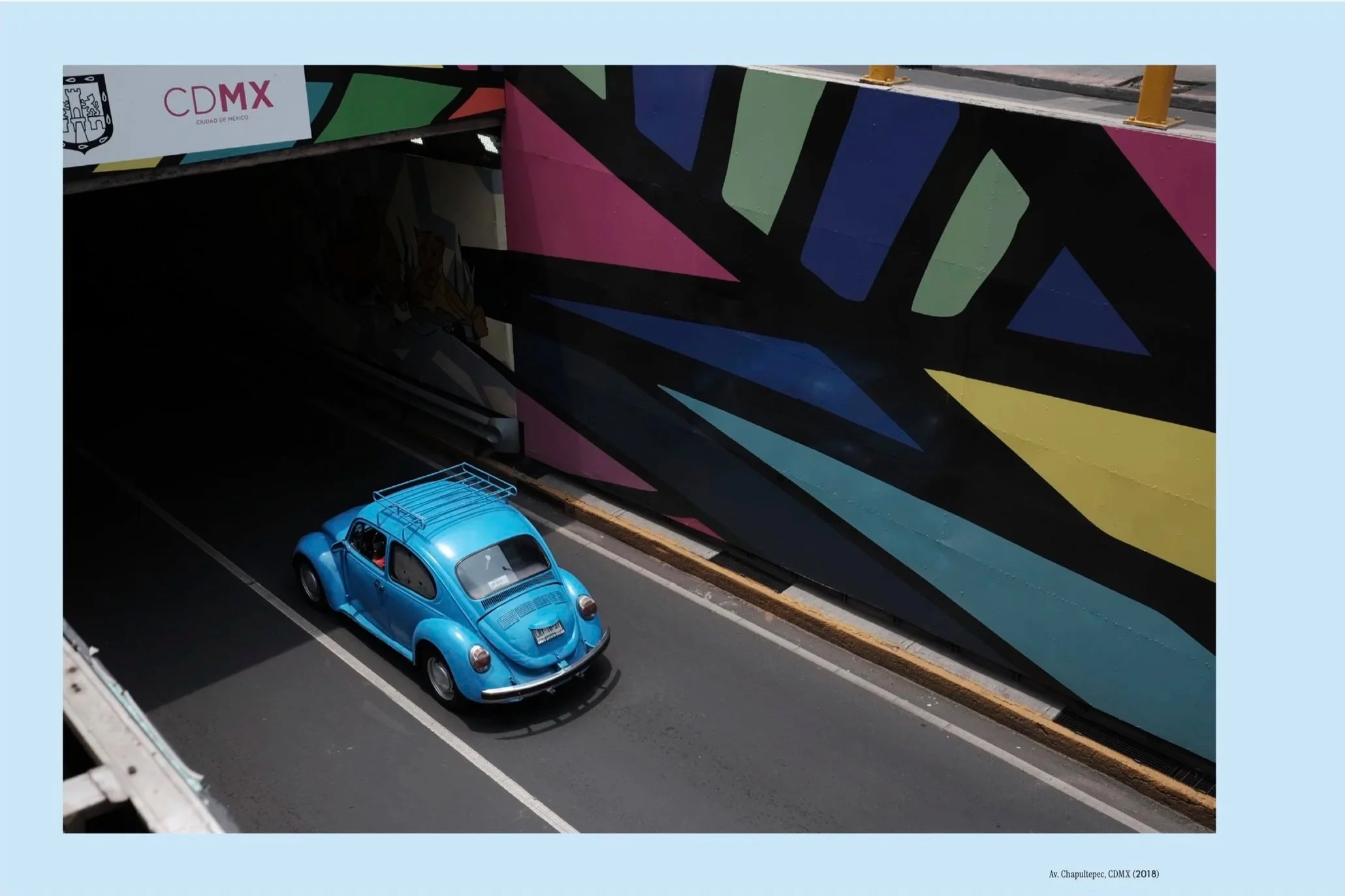 A blue Volkswagen Beetle drives into a tunnel in Mexico City surrounded by bright and vibrant murals. The image is part of the automotive photobook Vochos Unidos by Rodrigo Gaya Villar, published by Carrara Media (2026).