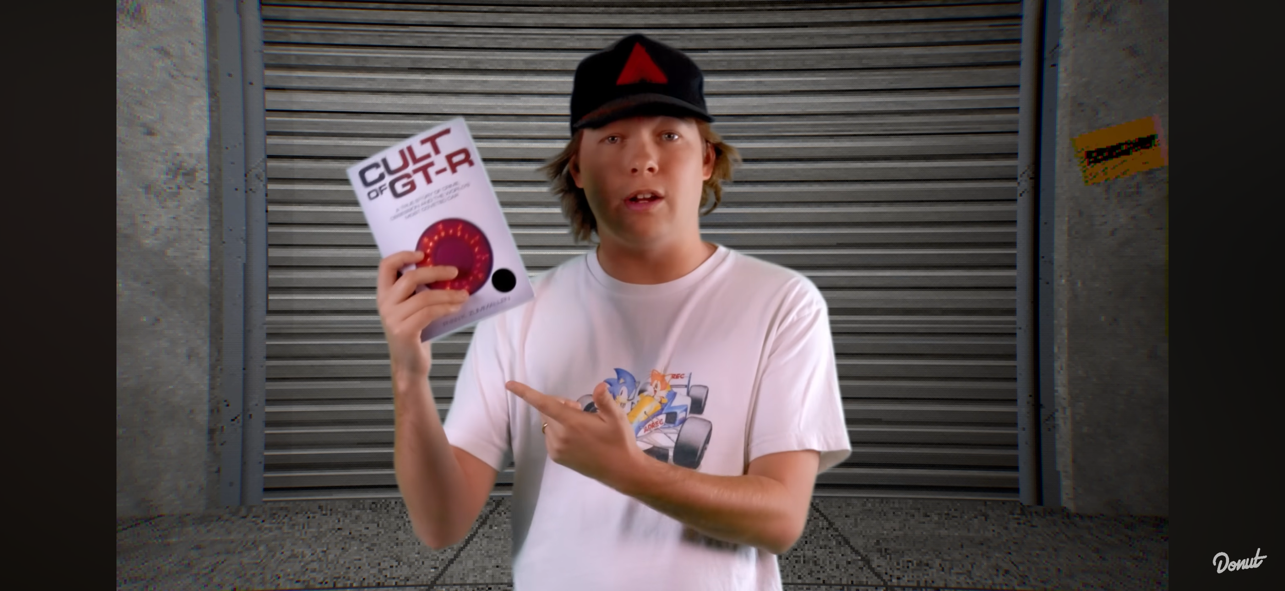 Jimmy Hilton of Donut Media holds a copy of the book 'Cult of GT-R' published by Carrara Media during a video about the Nissan Skyline GT-R and its notorious crime and controversial status in car culture.