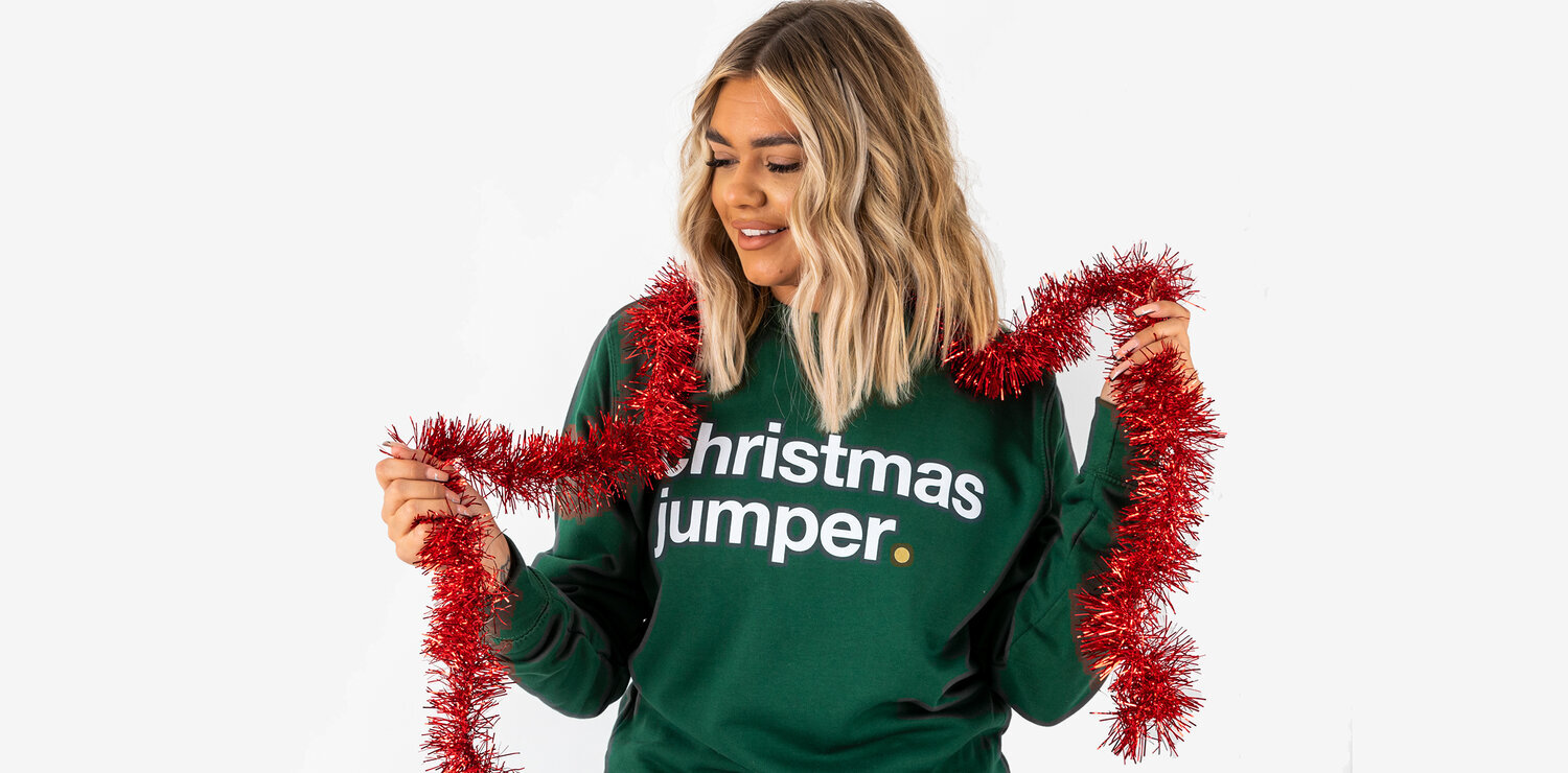 Woman wearing green christmas jumper holding tinsel