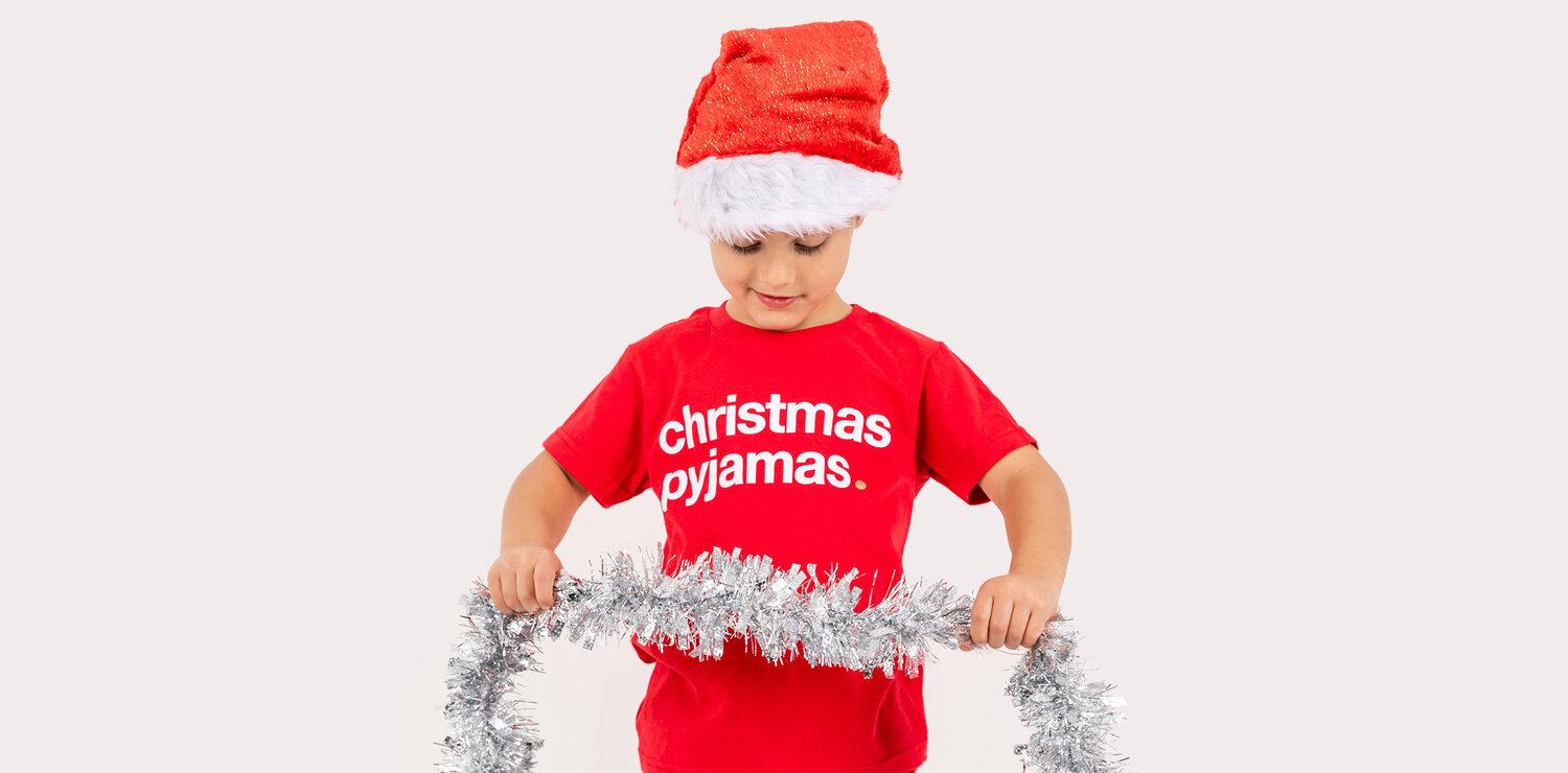 boy wearing red jumper wearing christmas hat and holding tinsel