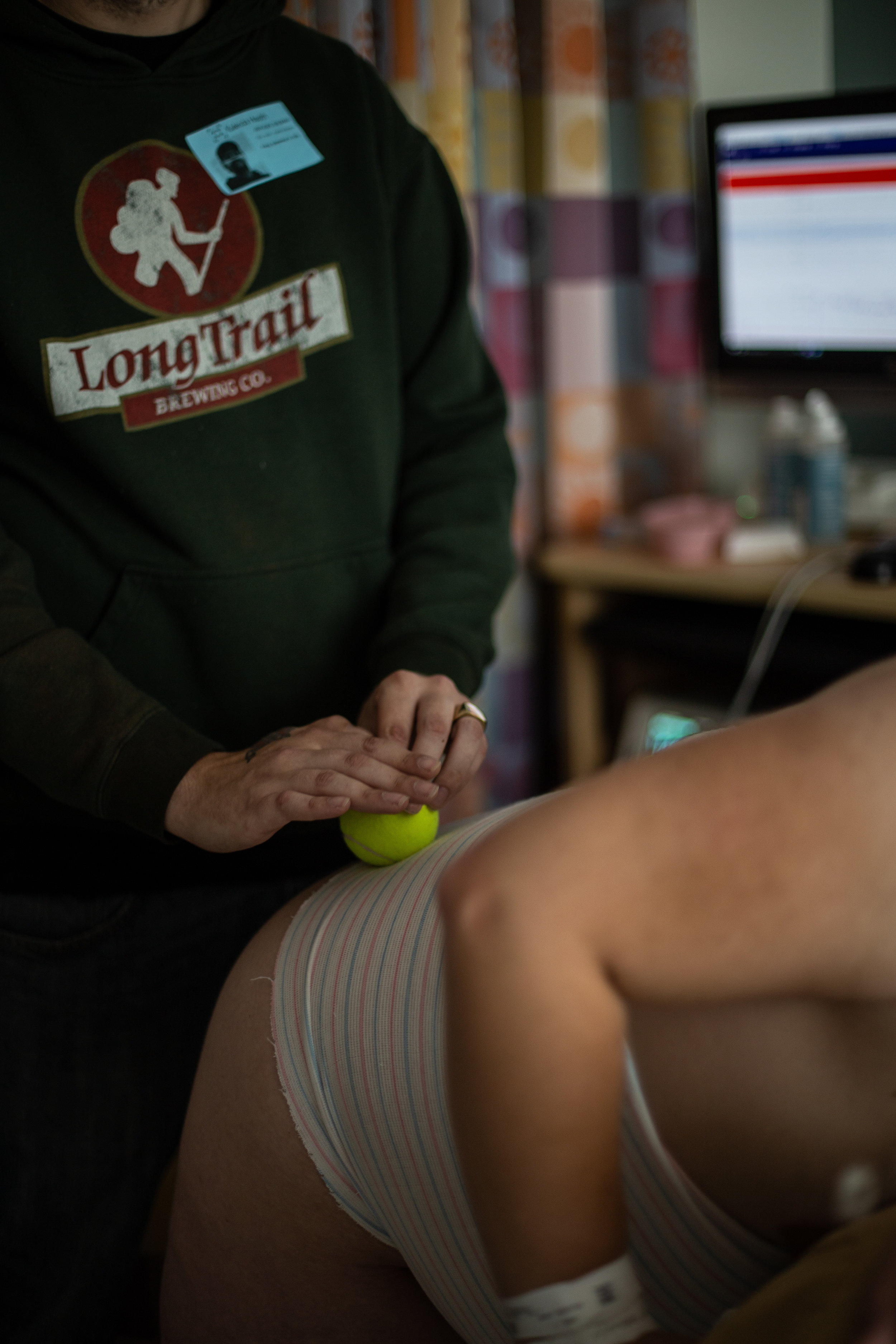 Man rolling a tennis ball on his wife's back while she labors leaning against the hospital bed.