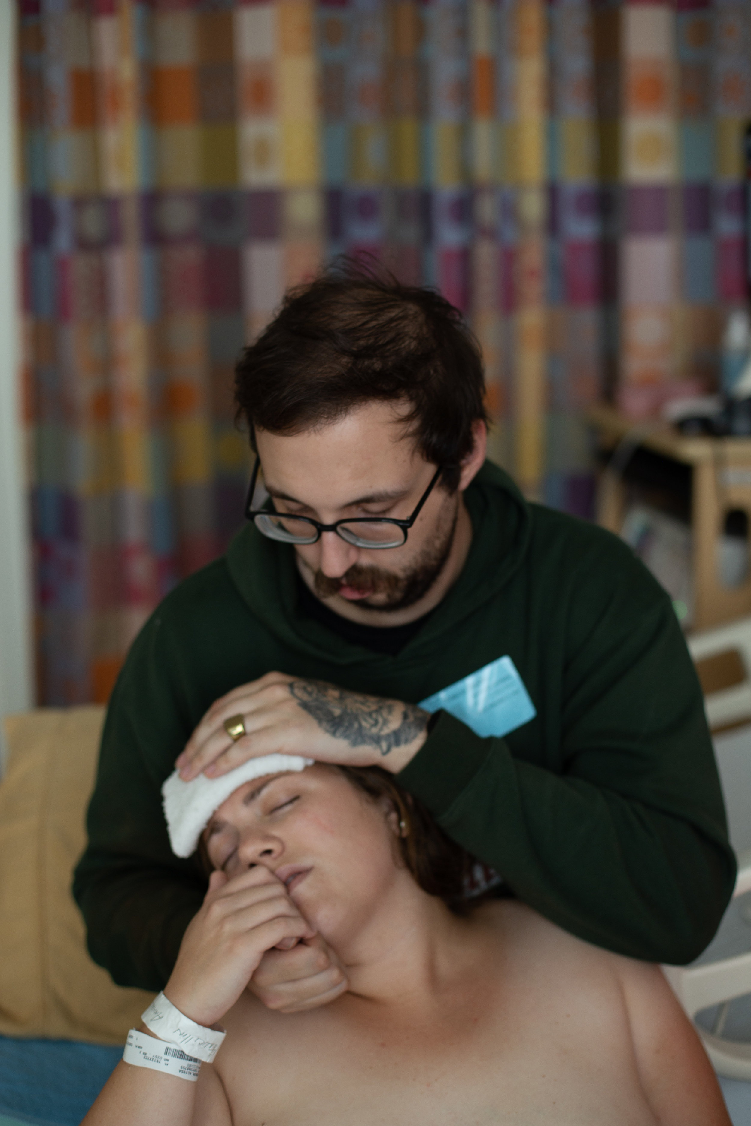 Man places cold washcloth on his partner's head while she rests.