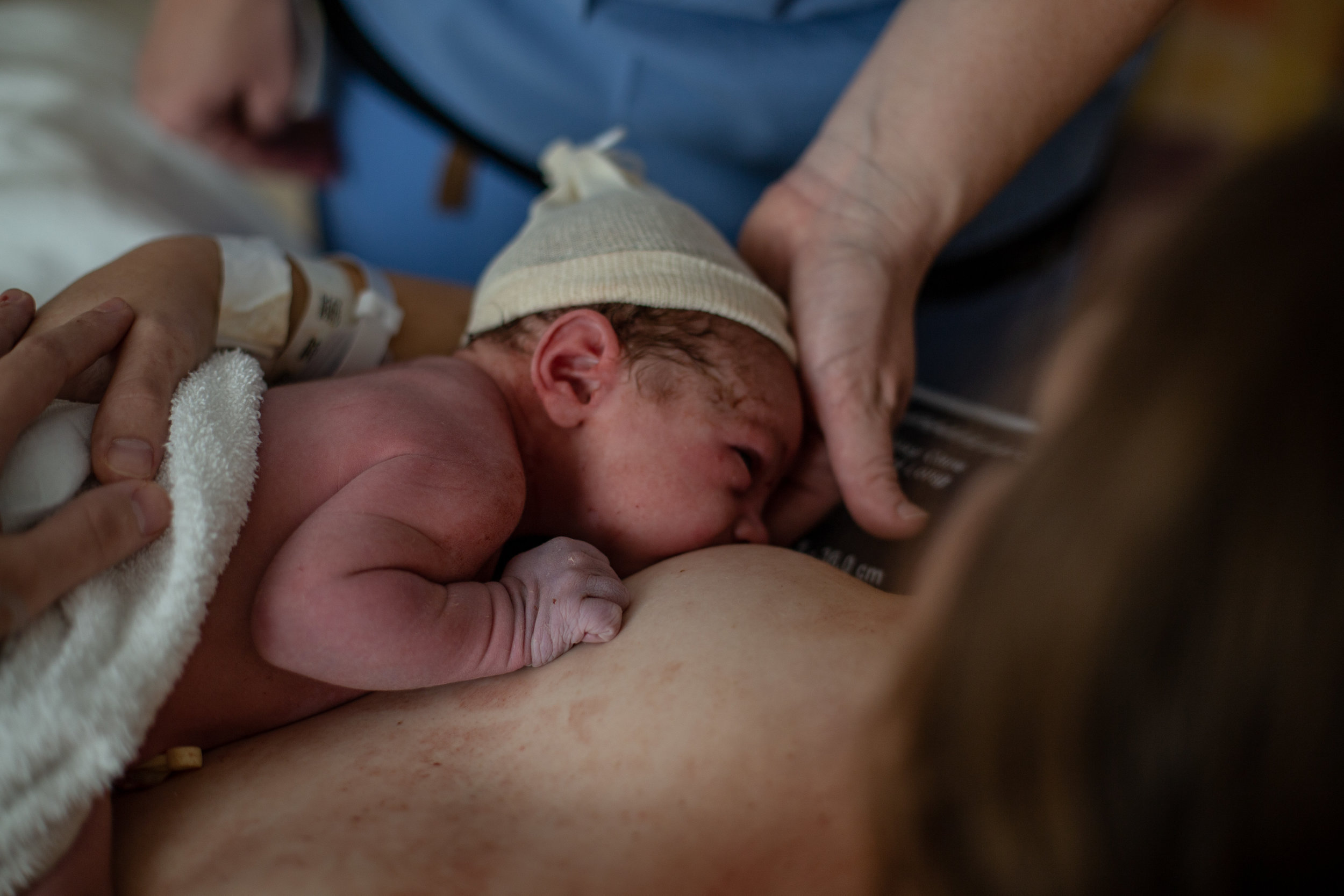 A nurse holds a newborn baby's head up to his mother's breast.