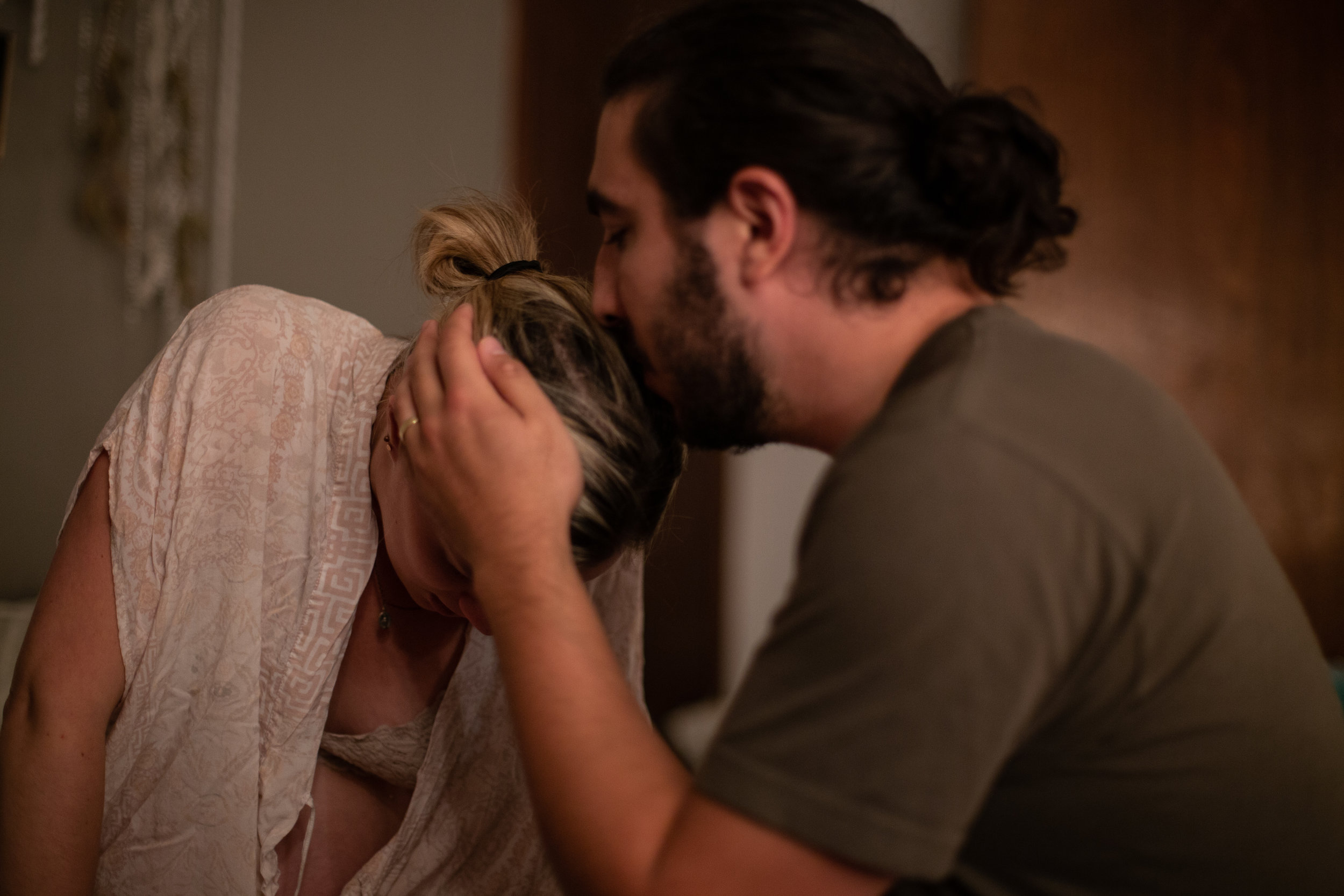 Husband kissing his wife on the top of her head while she is in labor.