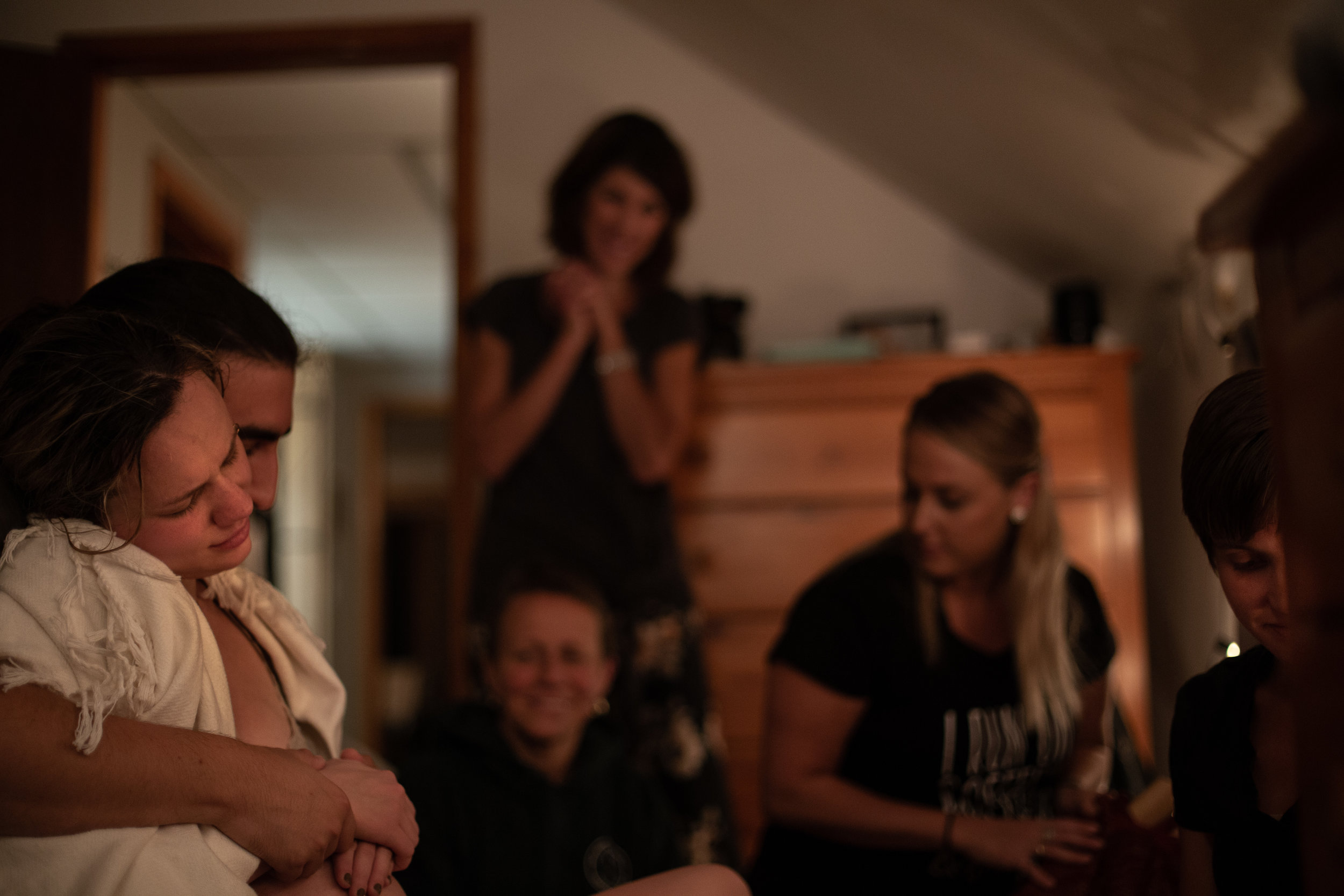 Six people smiling while a laboring mother sits on a birthing stool.