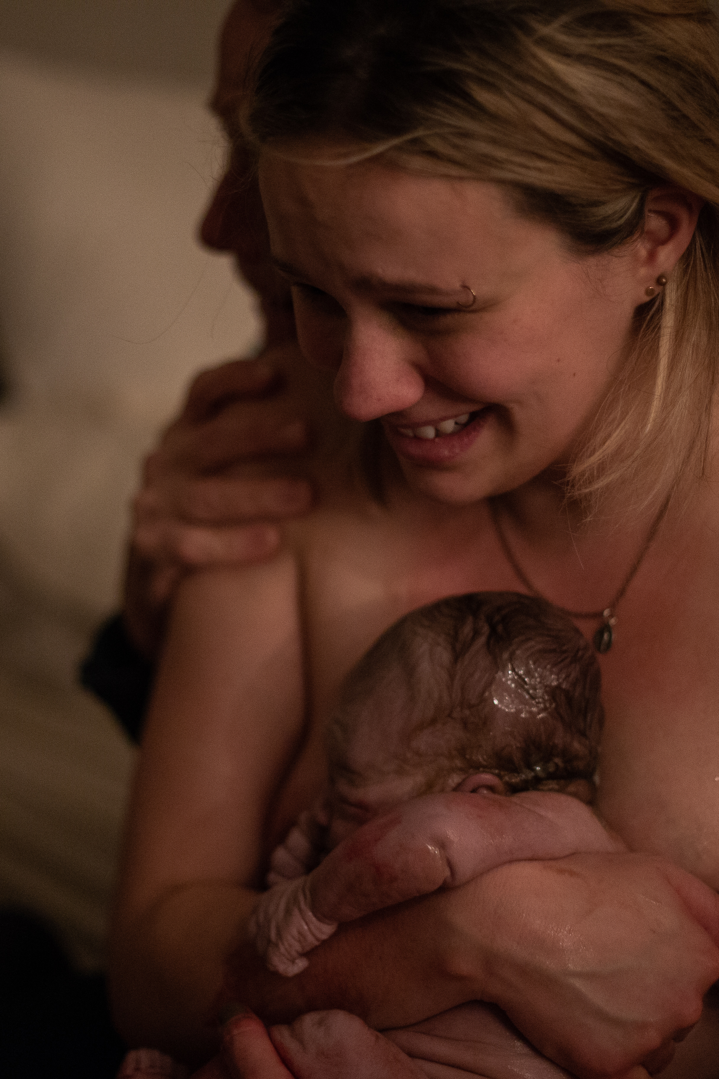A new mother holds her baby for the first time and smiles widely. 