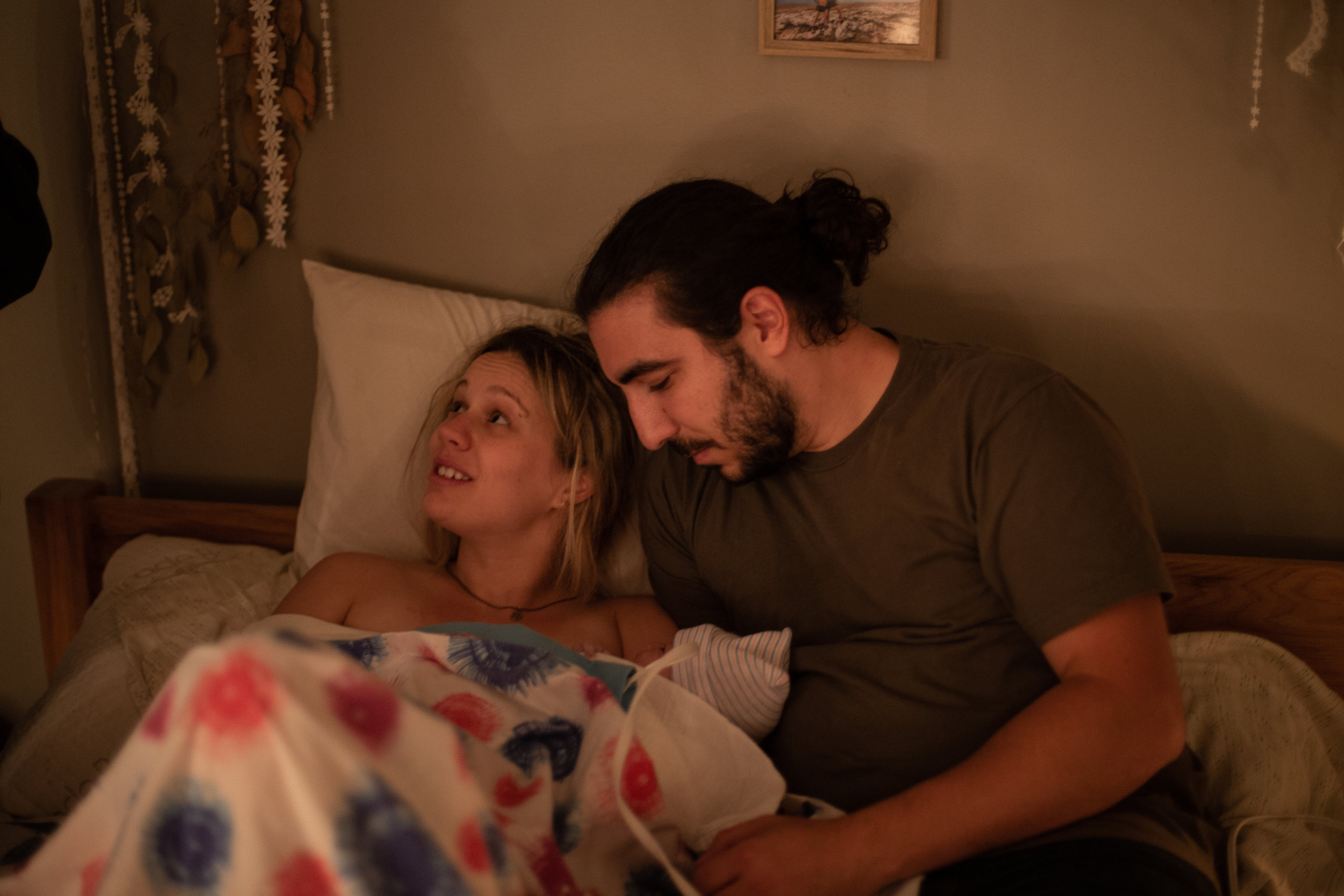 A new mom and dad snuggle with their baby in bed immediately after their home birth. 
