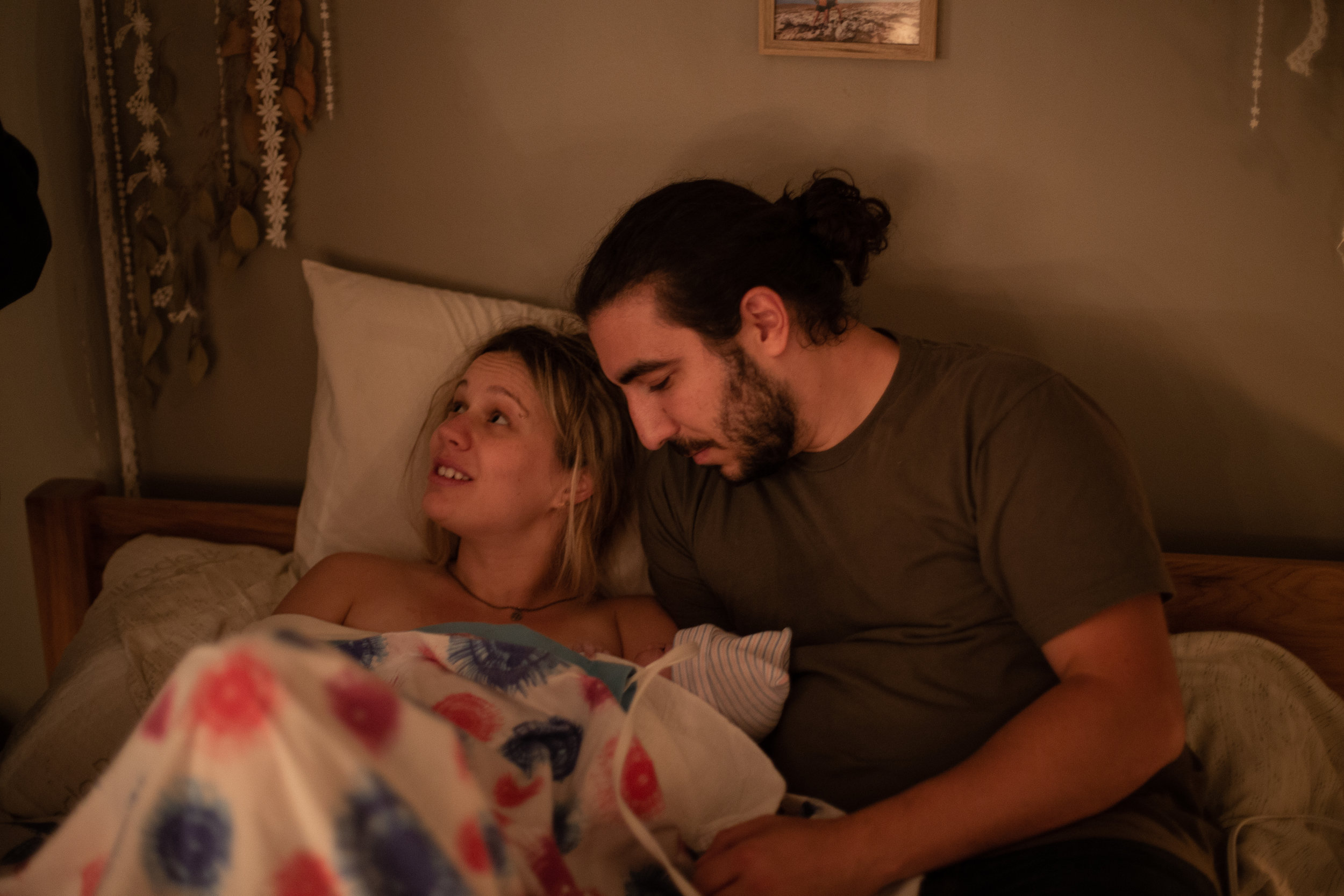 A new mom and dad snuggle with their baby in bed immediately after their home birth.