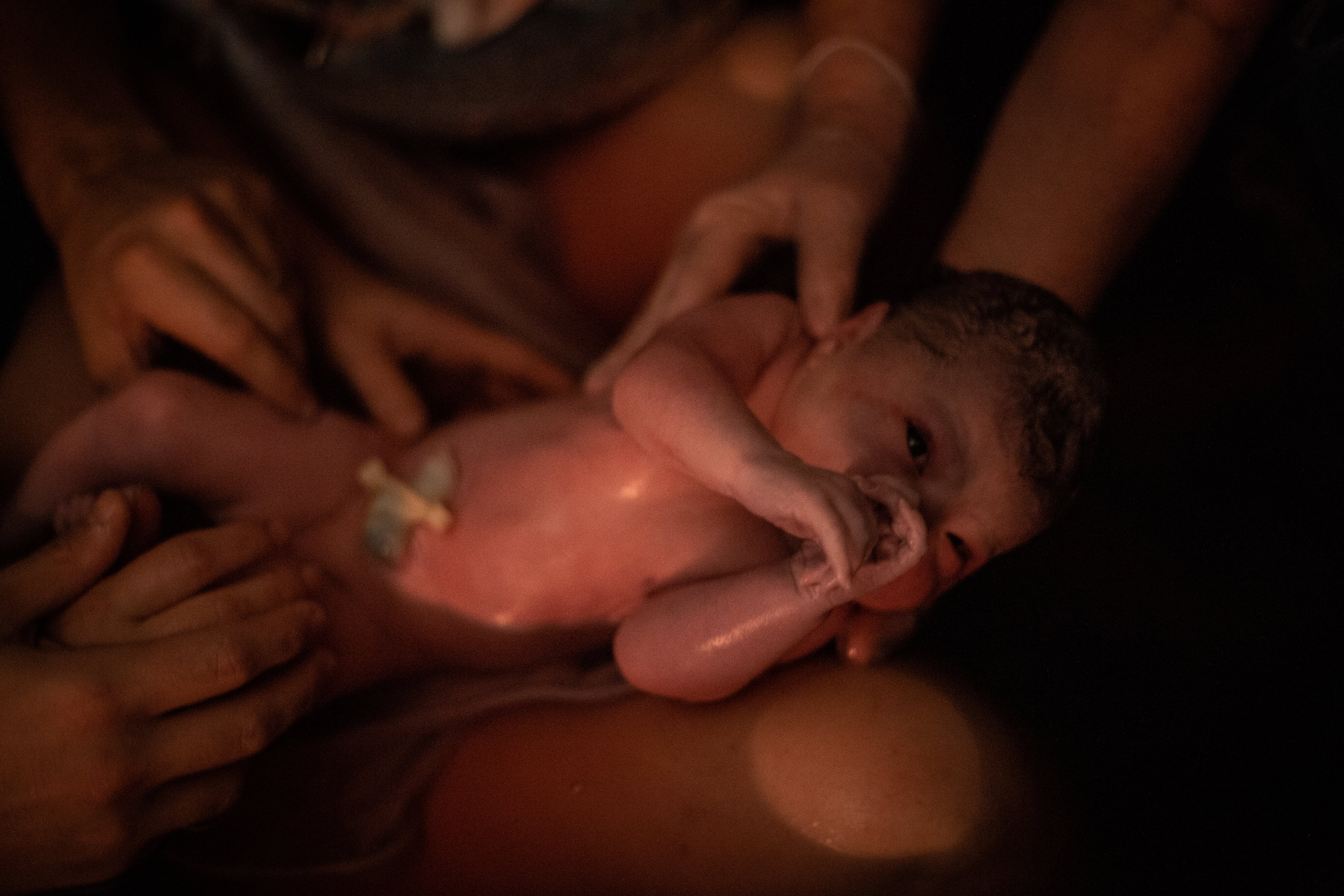 Many hands holding a baby floating in water.