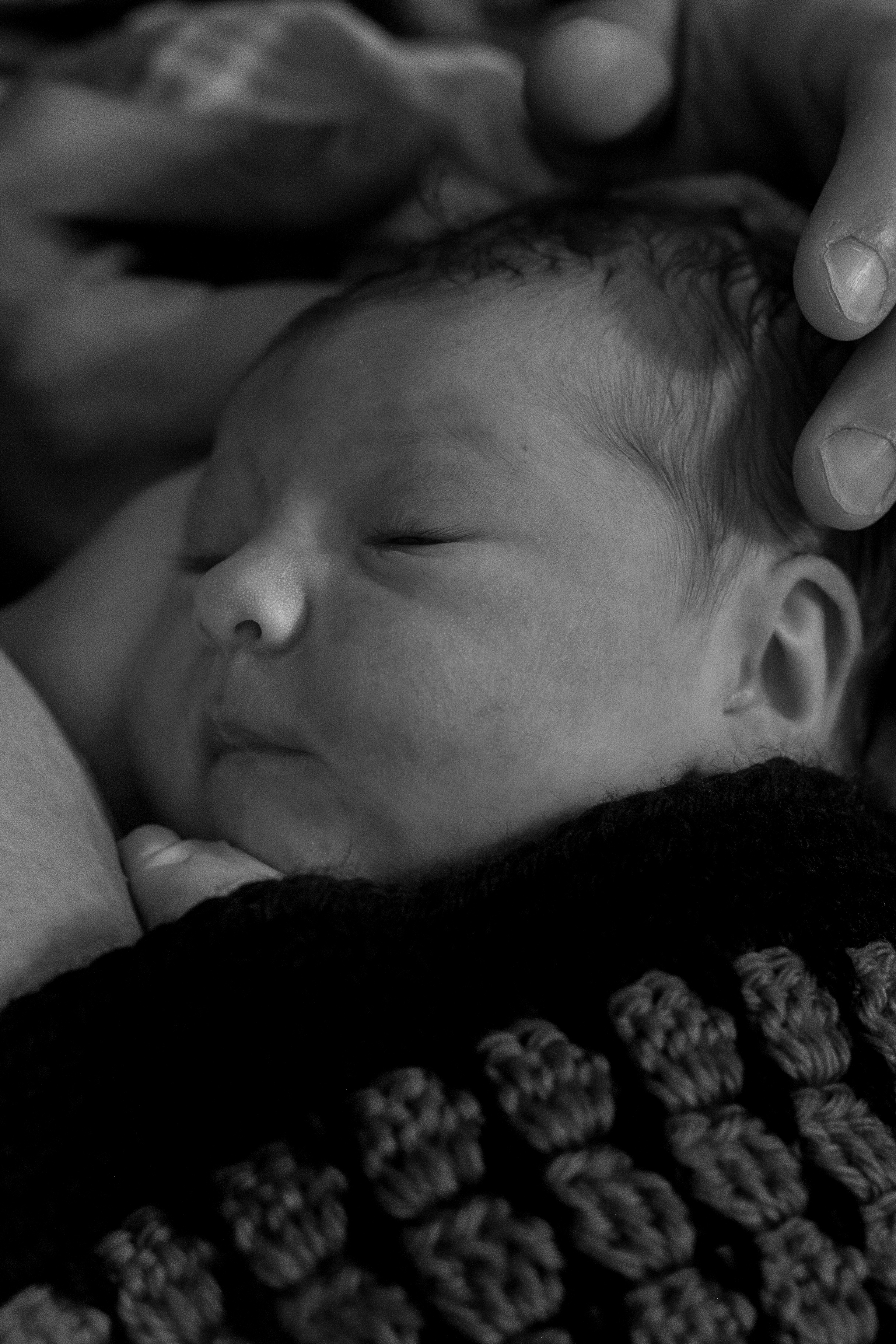 Black and white image of a newborn covered in a hand crocheted blanket. 