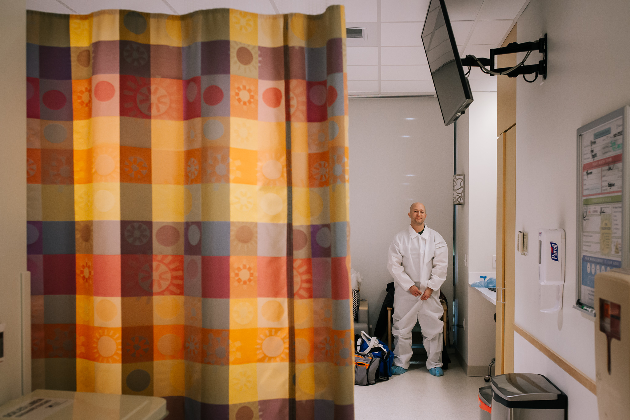 Man behind a hospital curtain gets a sterile suit on before a cesarean section.